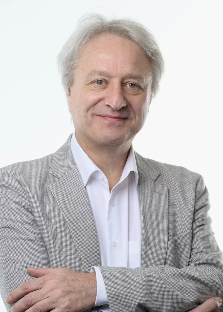 Portrait professionnel d'un homme portant un blazer gris à carreaux et une chemise blanche, les bras croisés, sur fond clair.