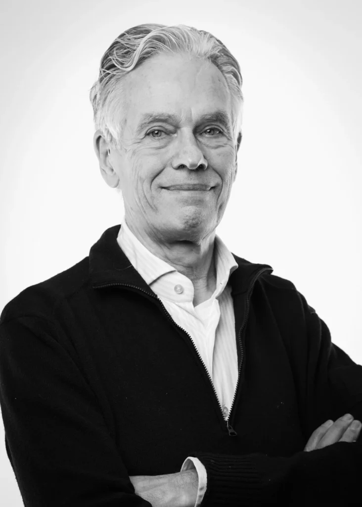 Black-and-white portrait of a man wearing a dark zip-up sweater over a white shirt, with his arms crossed.