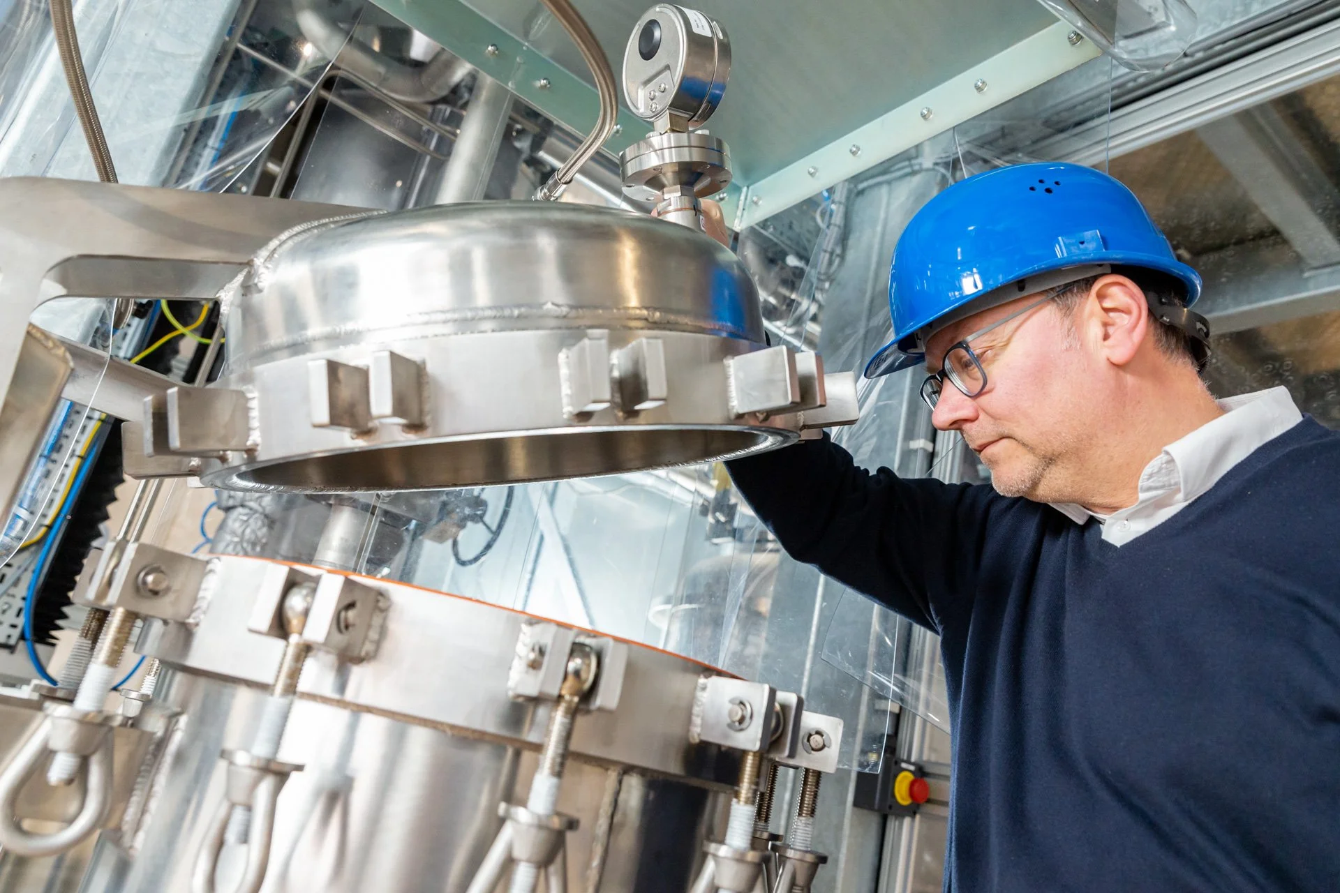 Photo d'entreprise d'un homme portant un casque de sécurité bleu inspectant une grande machine industrielle en métal.