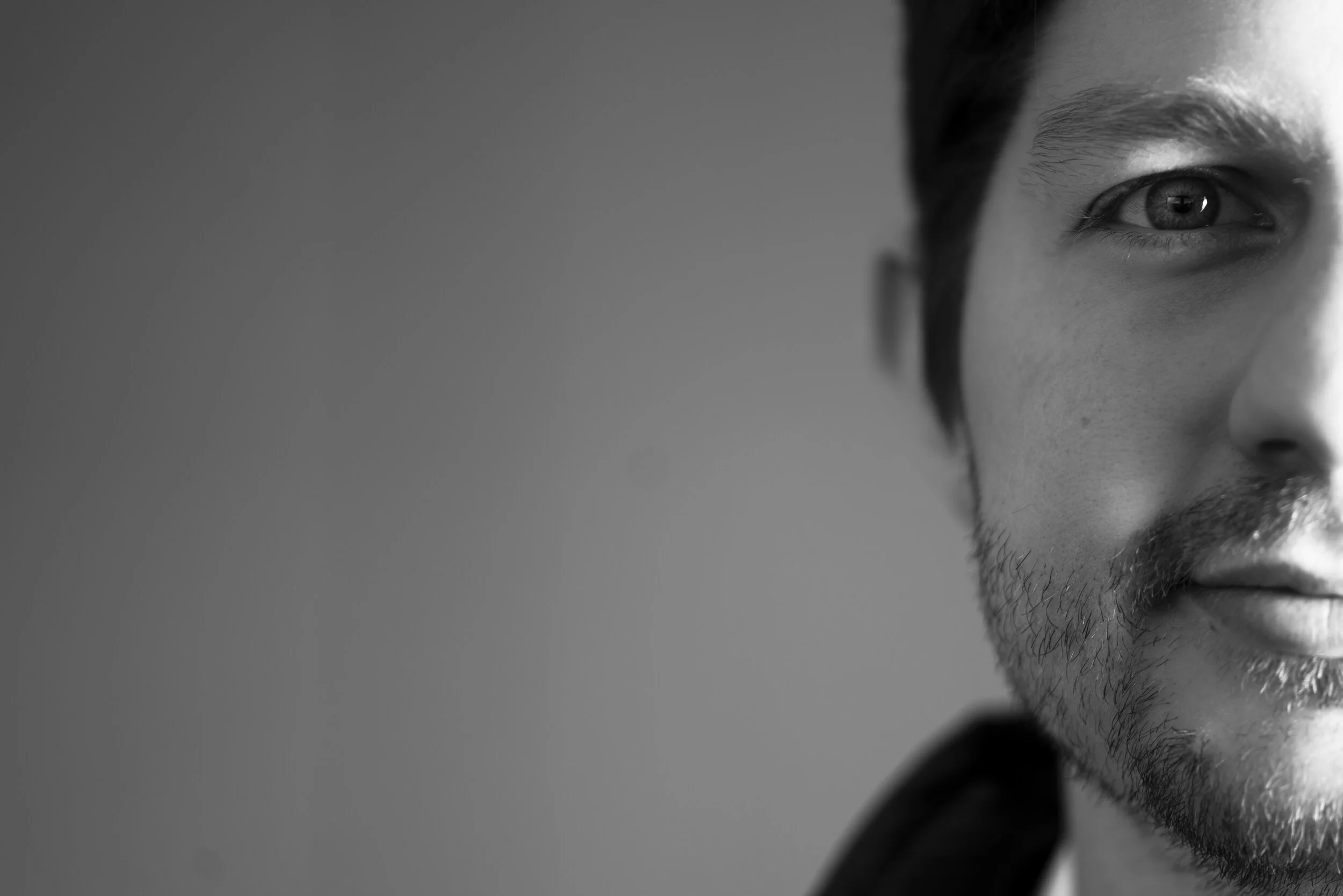 Black-and-white close-up showing one side of a man's face against a plain background.