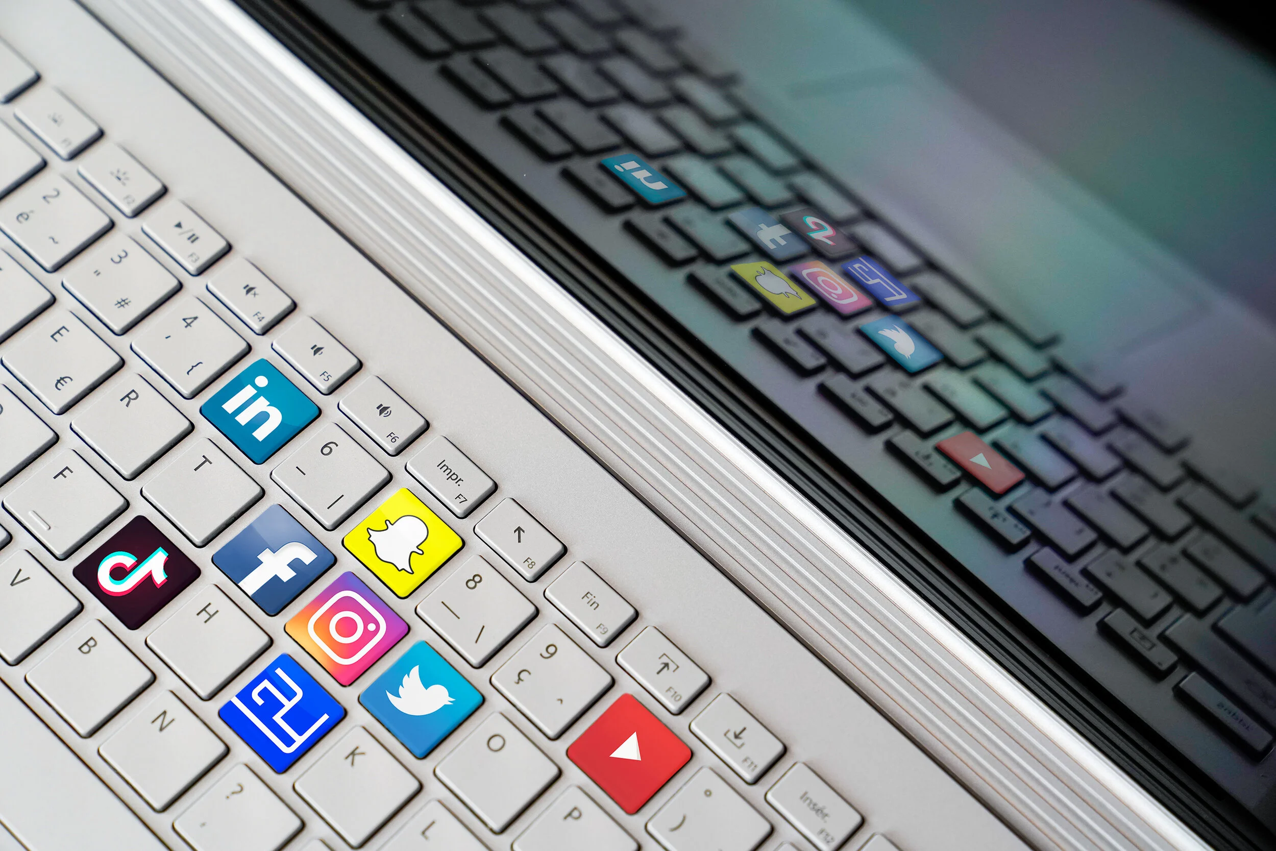 White laptop keyboard featuring colorful social media stickers including Facebook, Instagram, and LinkedIn.