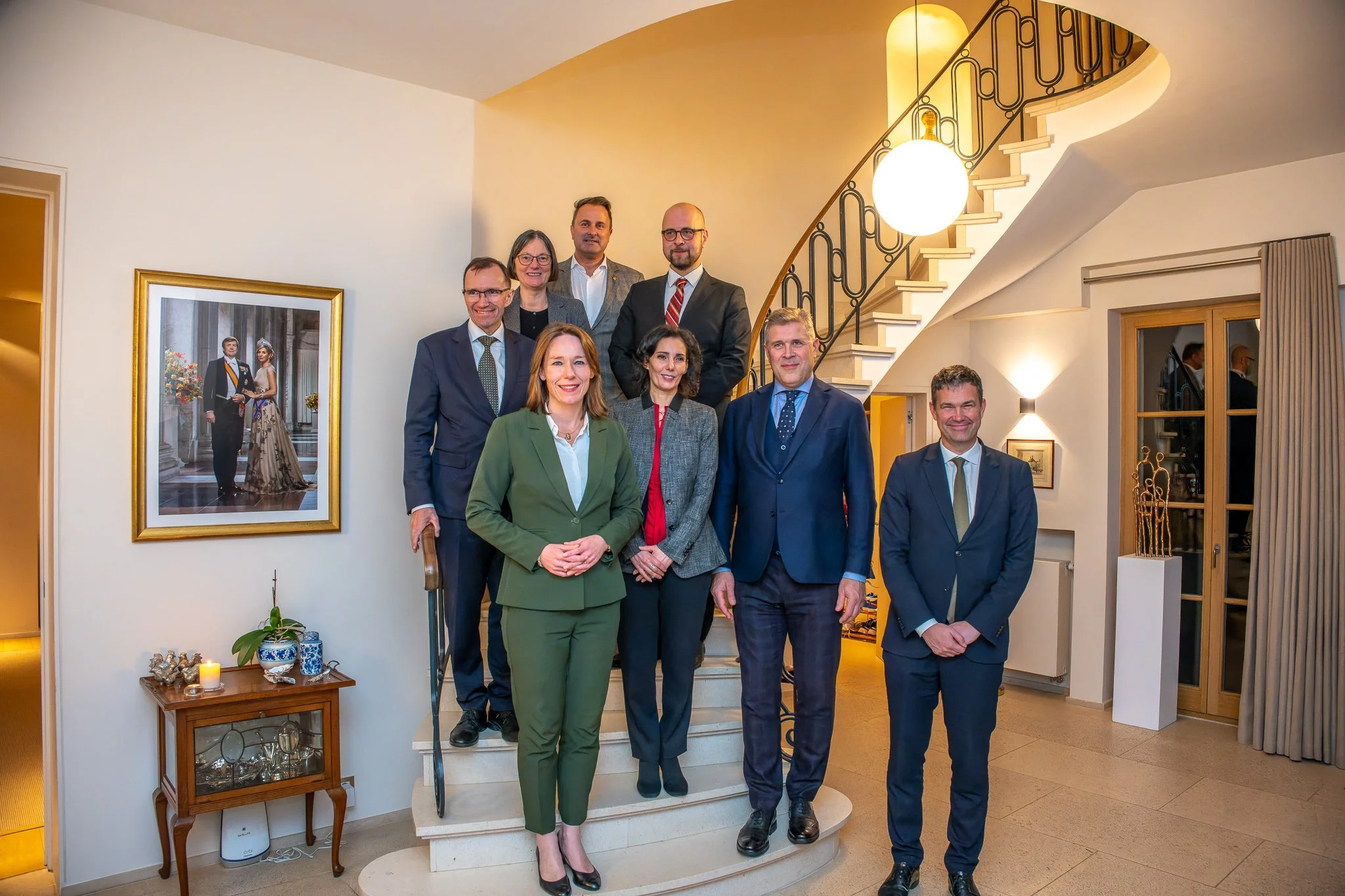 A group of people in business attire pose beside a staircase in an elegant interior.