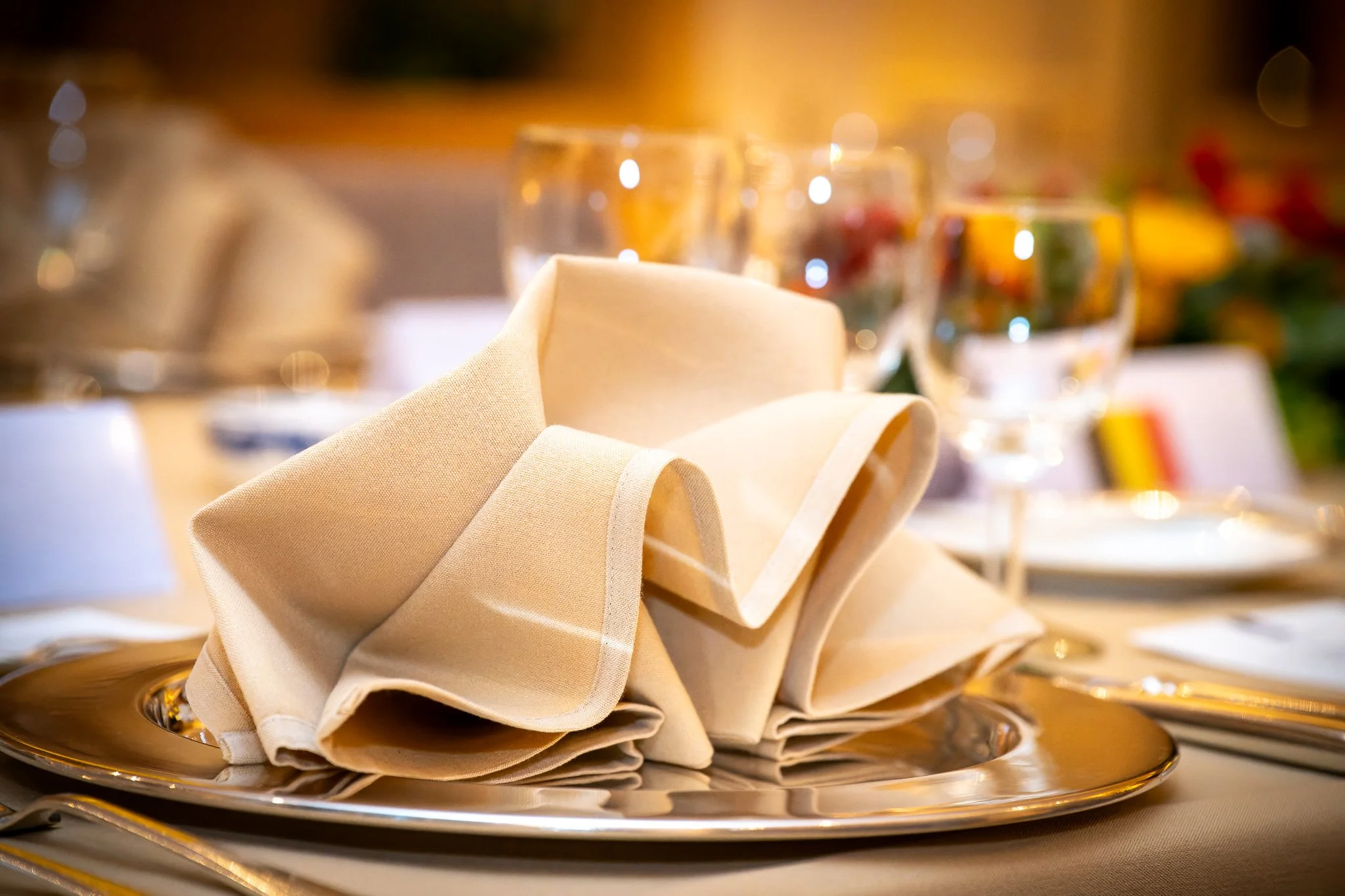 Folded napkin on a plate, with glasses on a laid table.