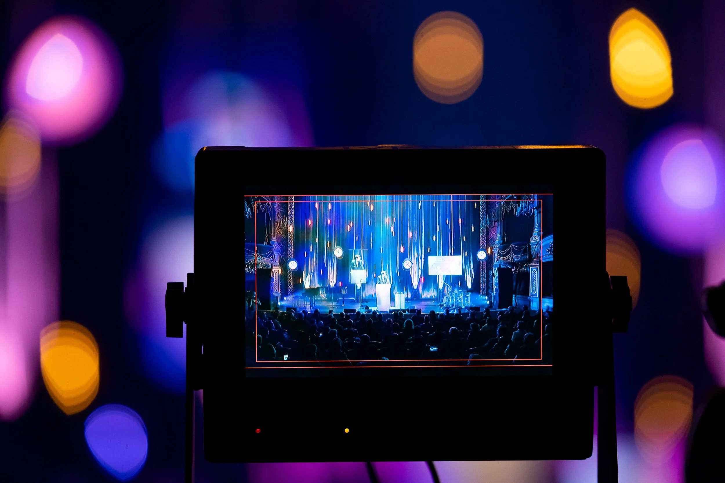 A camera screen shows a concert scene, with blurred coloured lights in the background.