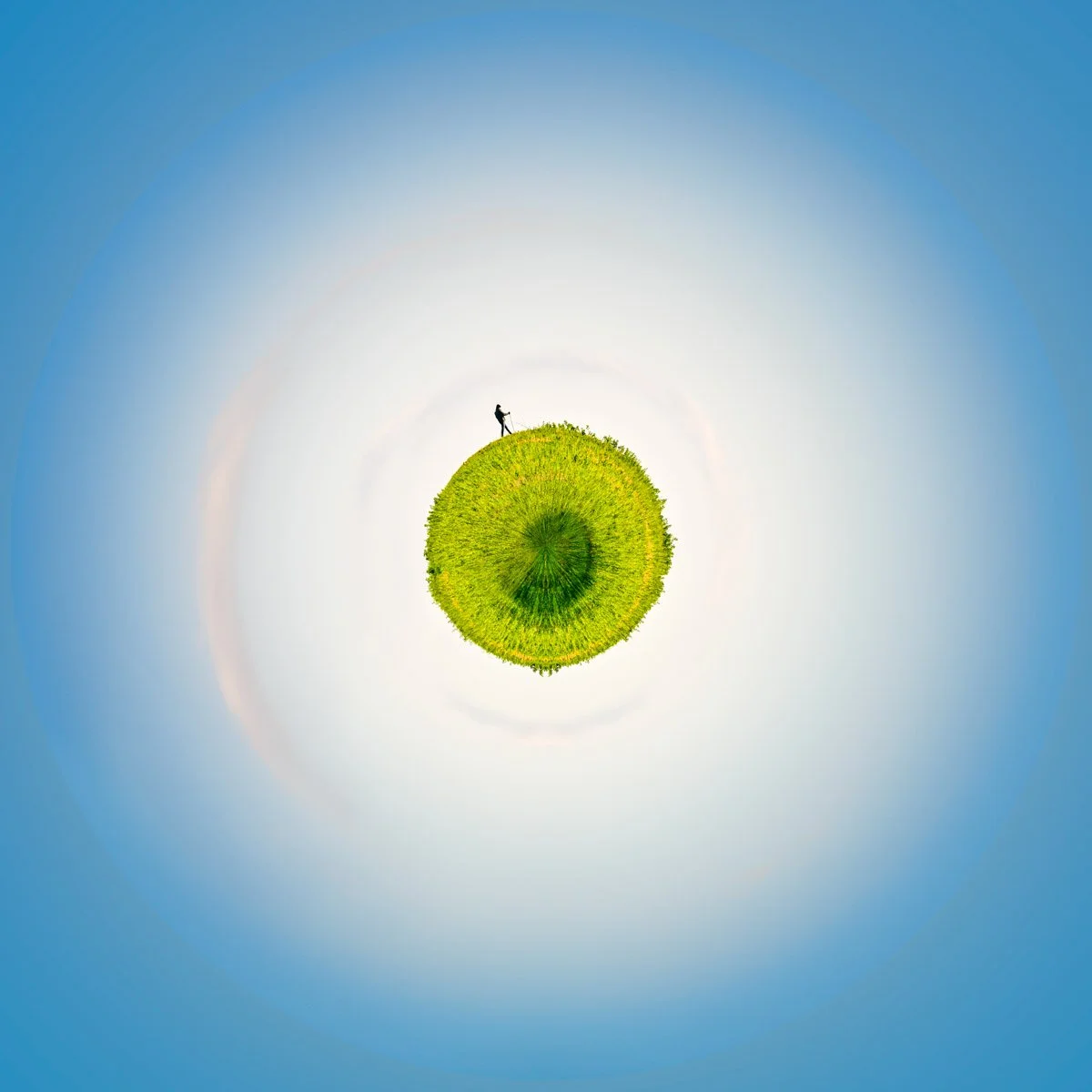 A small, green planet surrounded by a vast white halo and a blue sky, with a silhouette on its edge.