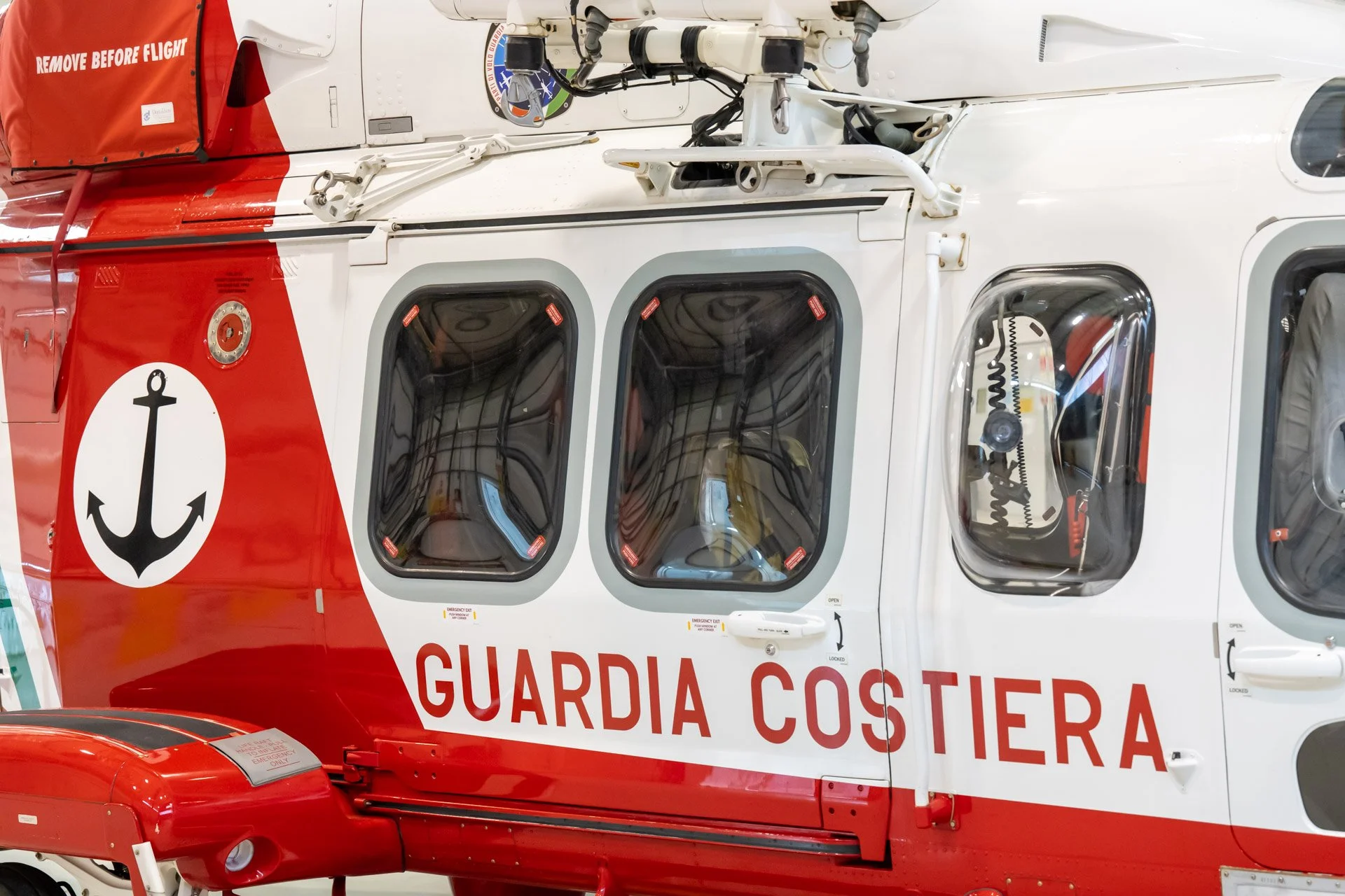 Vue rapprochée d'un hélicoptère de la Guardia Costiera, avec une ancre noire sur fond blanc et la mention "Remove Before Flight".