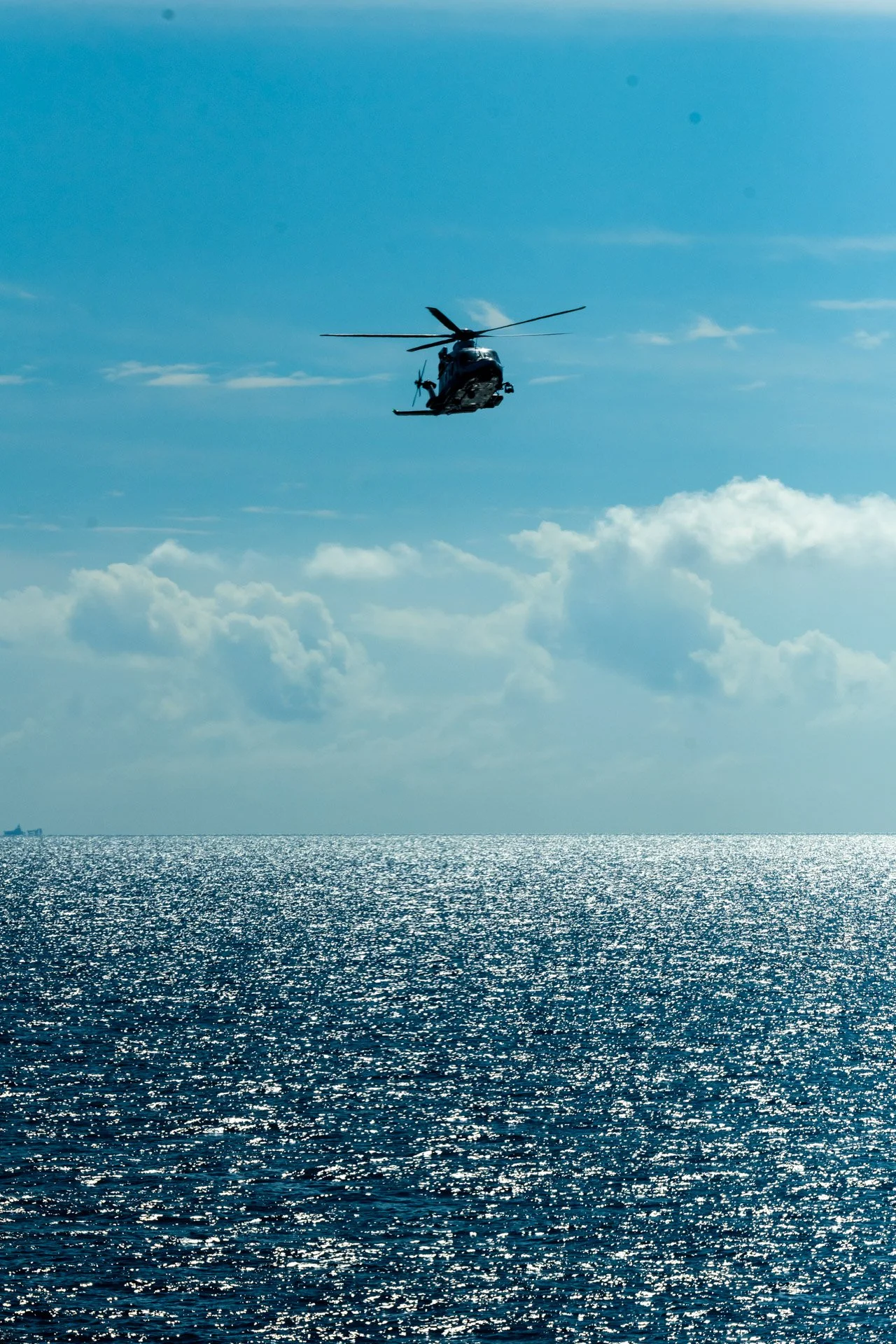 Hélicoptère volant au-dessus de la mer avec ciel bleu et nuages.