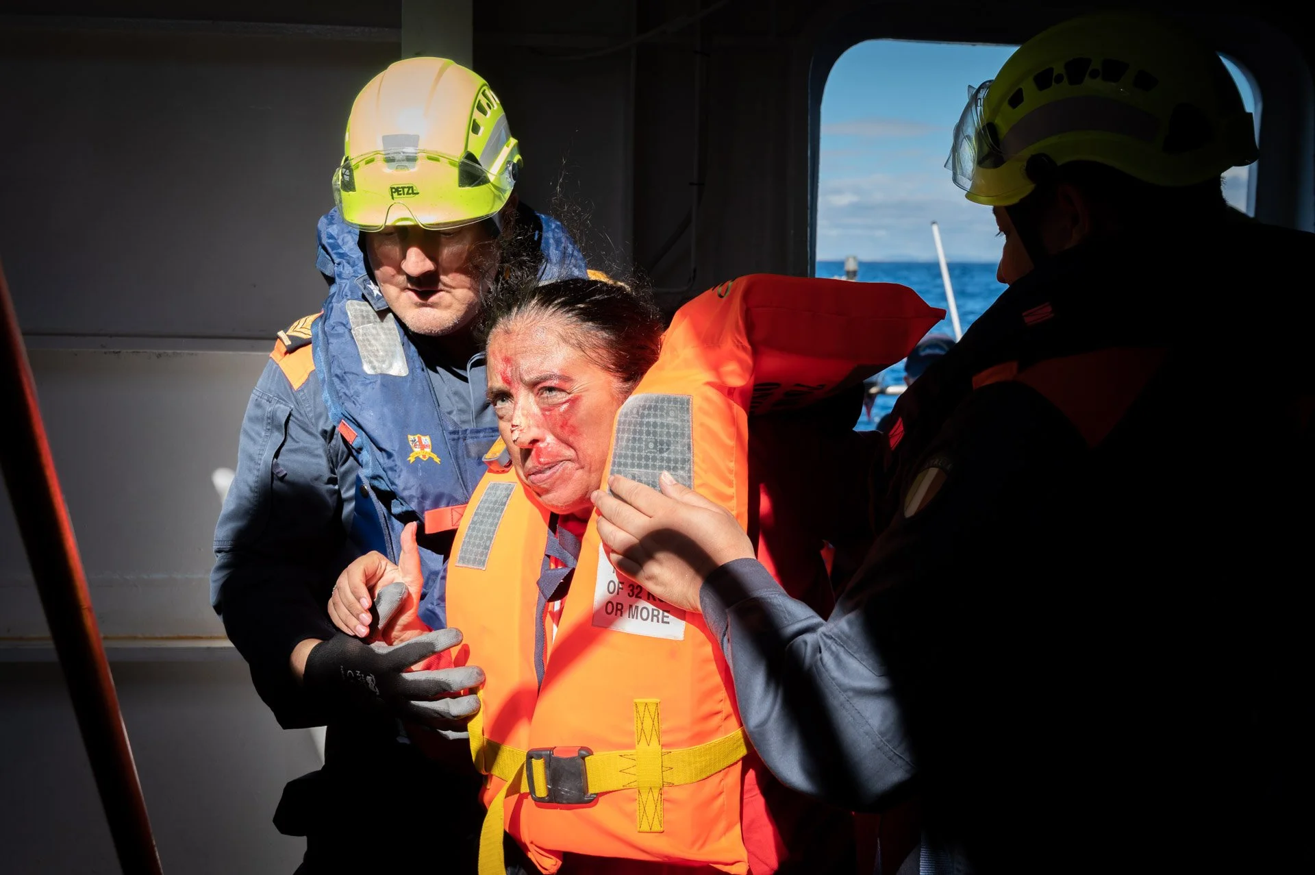 Une personne en gilet de sauvetage est aidée par des secouristes habillés en équipement de sauvetage maritime.