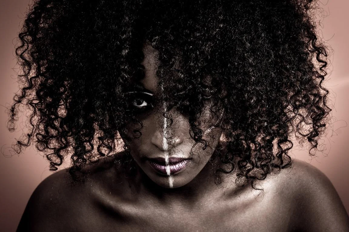 Portrait d'une personne avec des cheveux bouclés, un maquillage artistique et des motifs blancs sur le visage.
