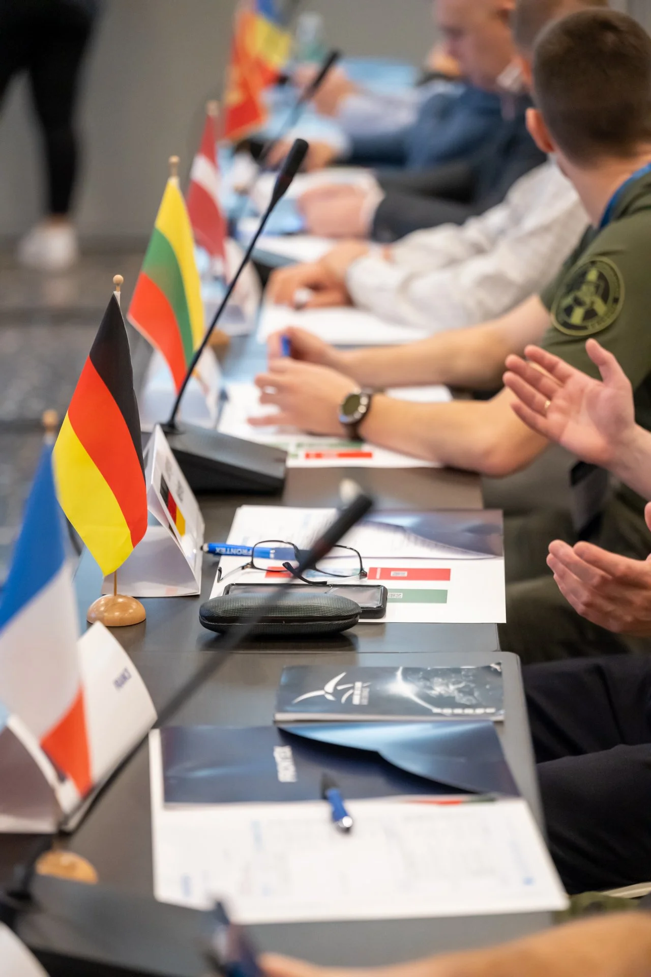 Réunion internationale avec des drapeaux de plusieurs pays sur une table, personnes discutant avec des documents et des micros.