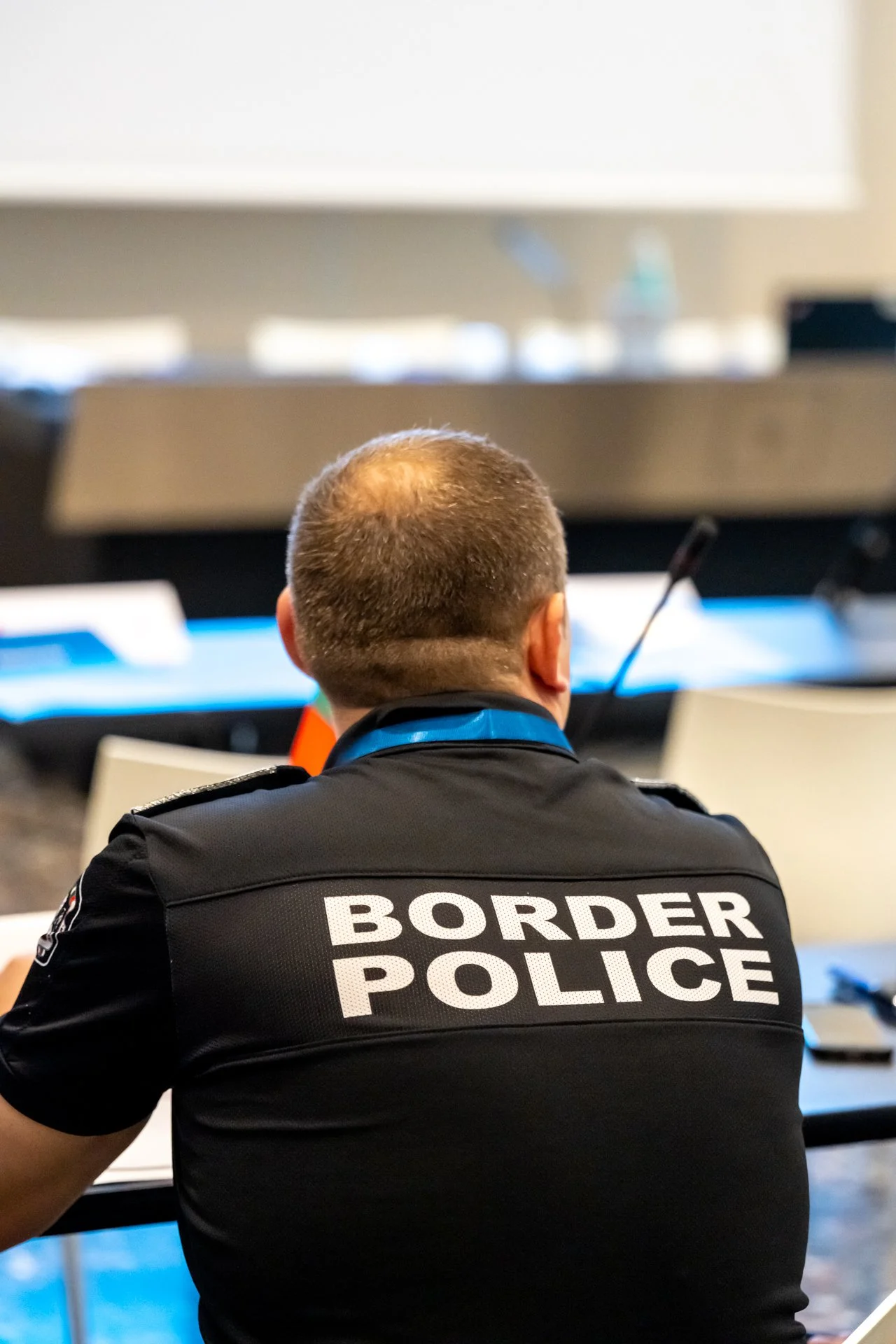 Un agent de la police des frontières vu de dos, portant un uniforme avec l'inscription "BORDER POLICE".