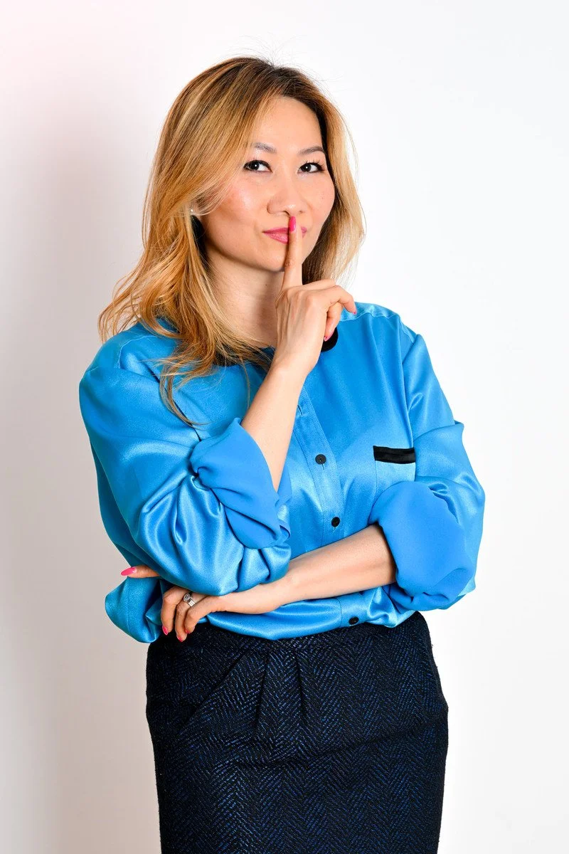 Femme en chemisier bleu avec un doigt sur les lèvres en signe de silence.