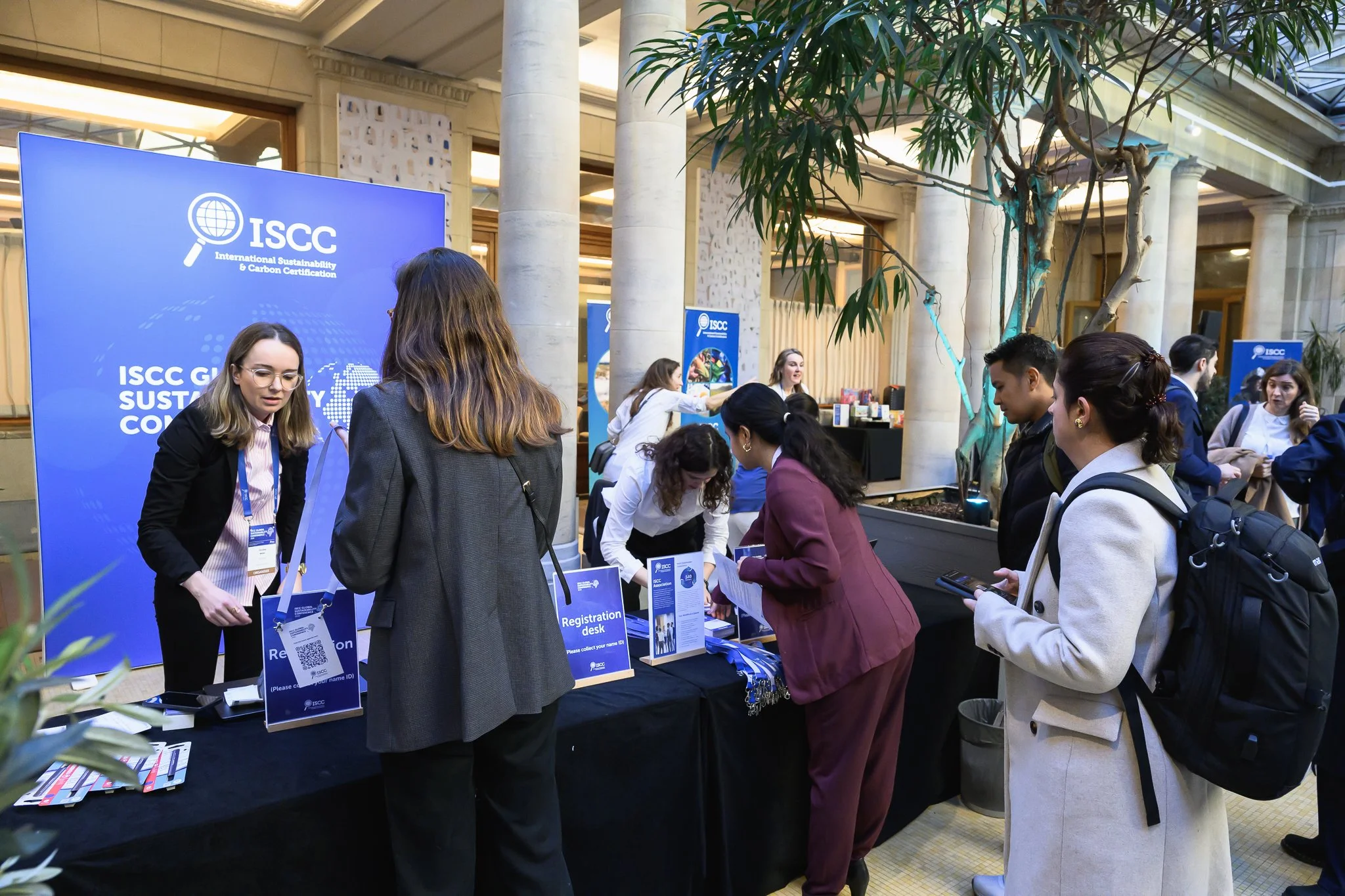Visitors collect conference badges at an ISCC registration desk in a bright lobby.