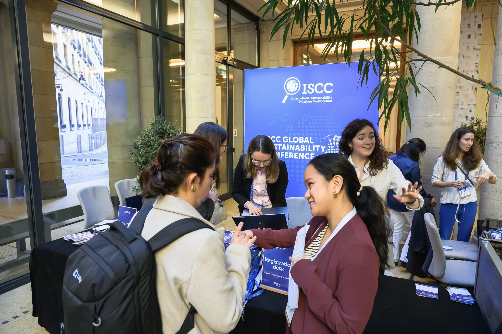 Conference staff talk with arriving visitors at the registration desk beneath blue ISCC banners.