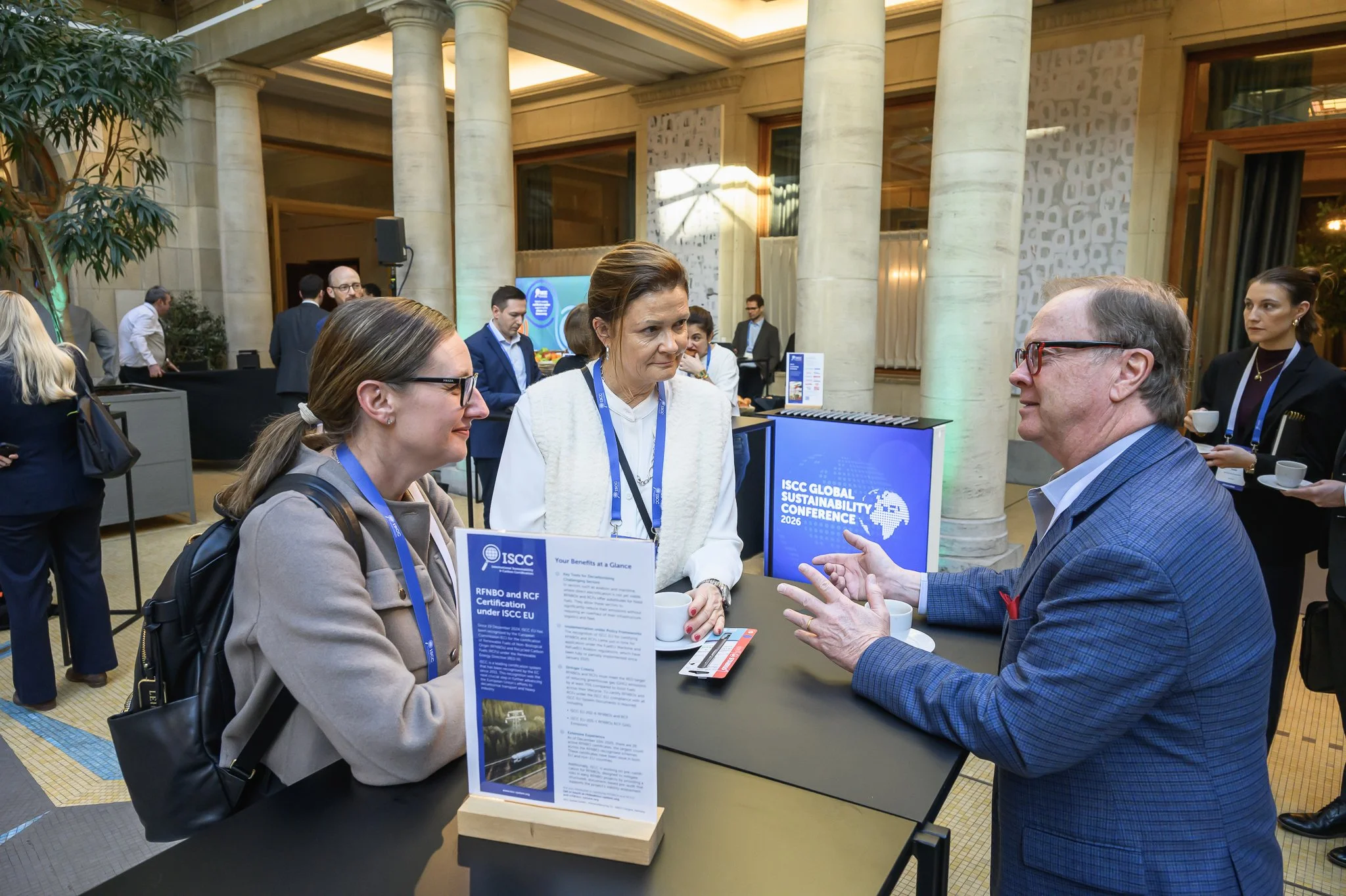 Three participants talk around a tall table with a conference information stand.