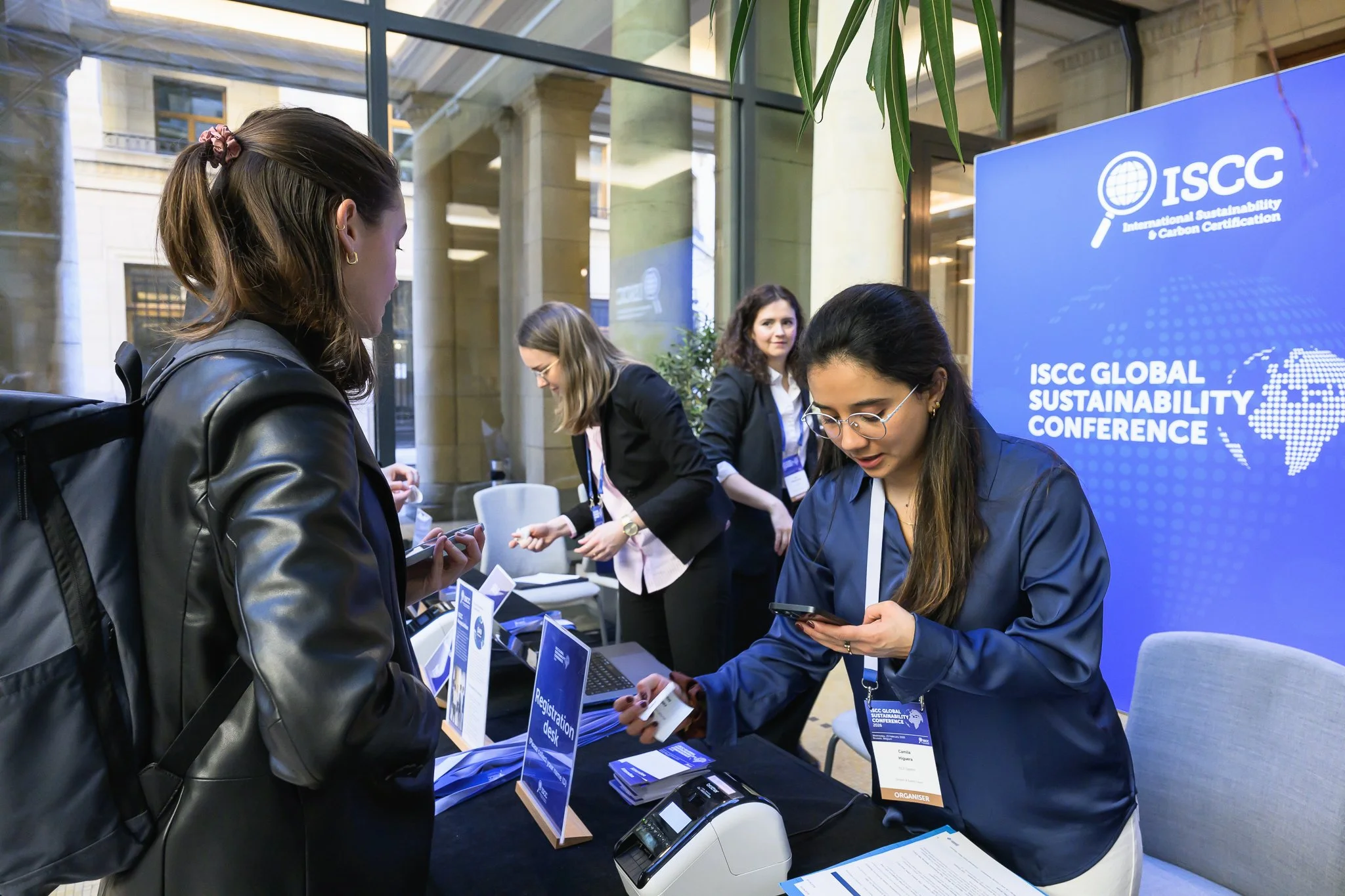 A staff member sorts badges at the registration desk while a visitor waits.