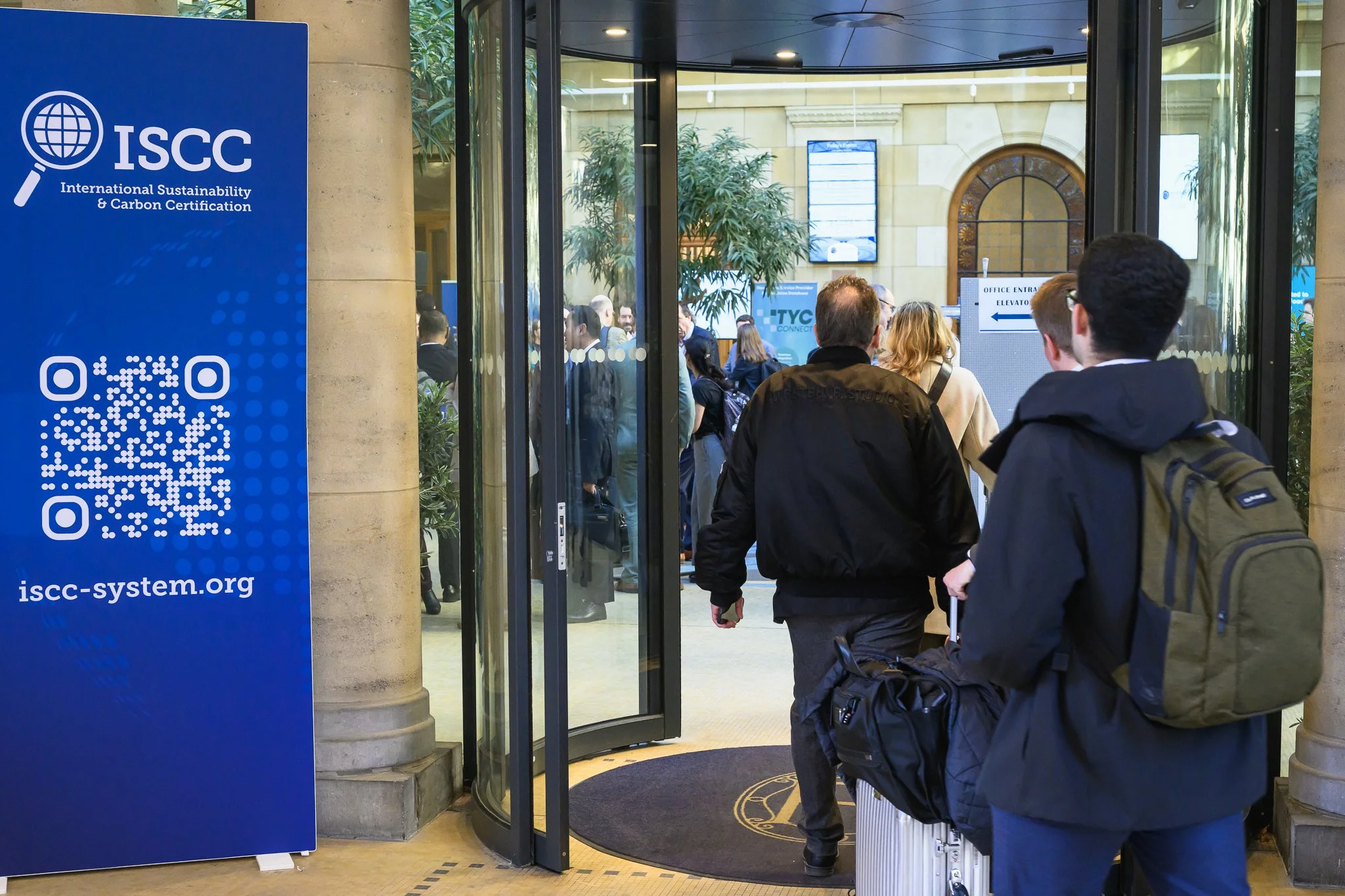 Visitors enter through glass doors beside an ISCC banner with a QR code.