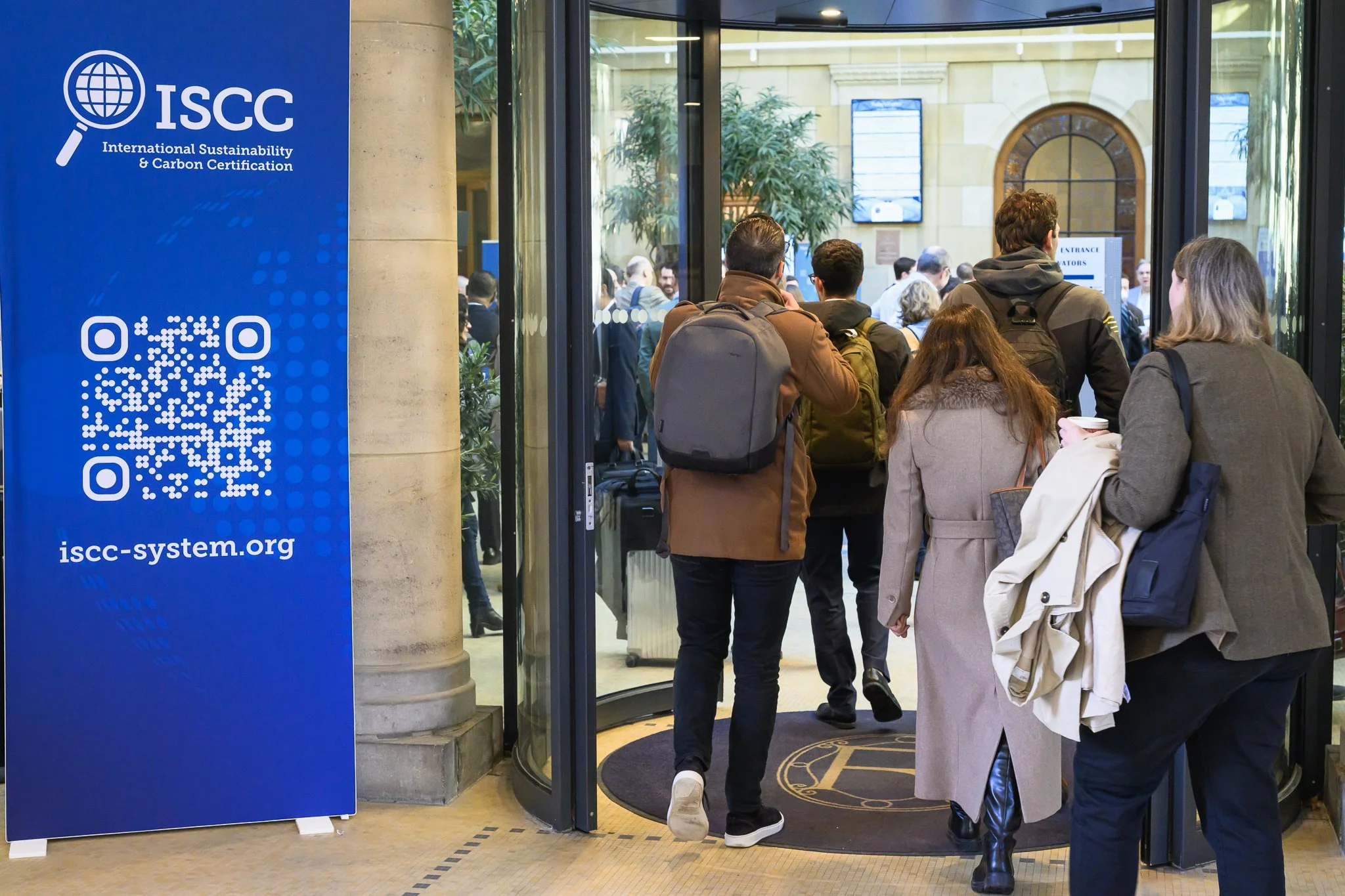 Visitors pass through the glass entrance beside a blue ISCC banner.