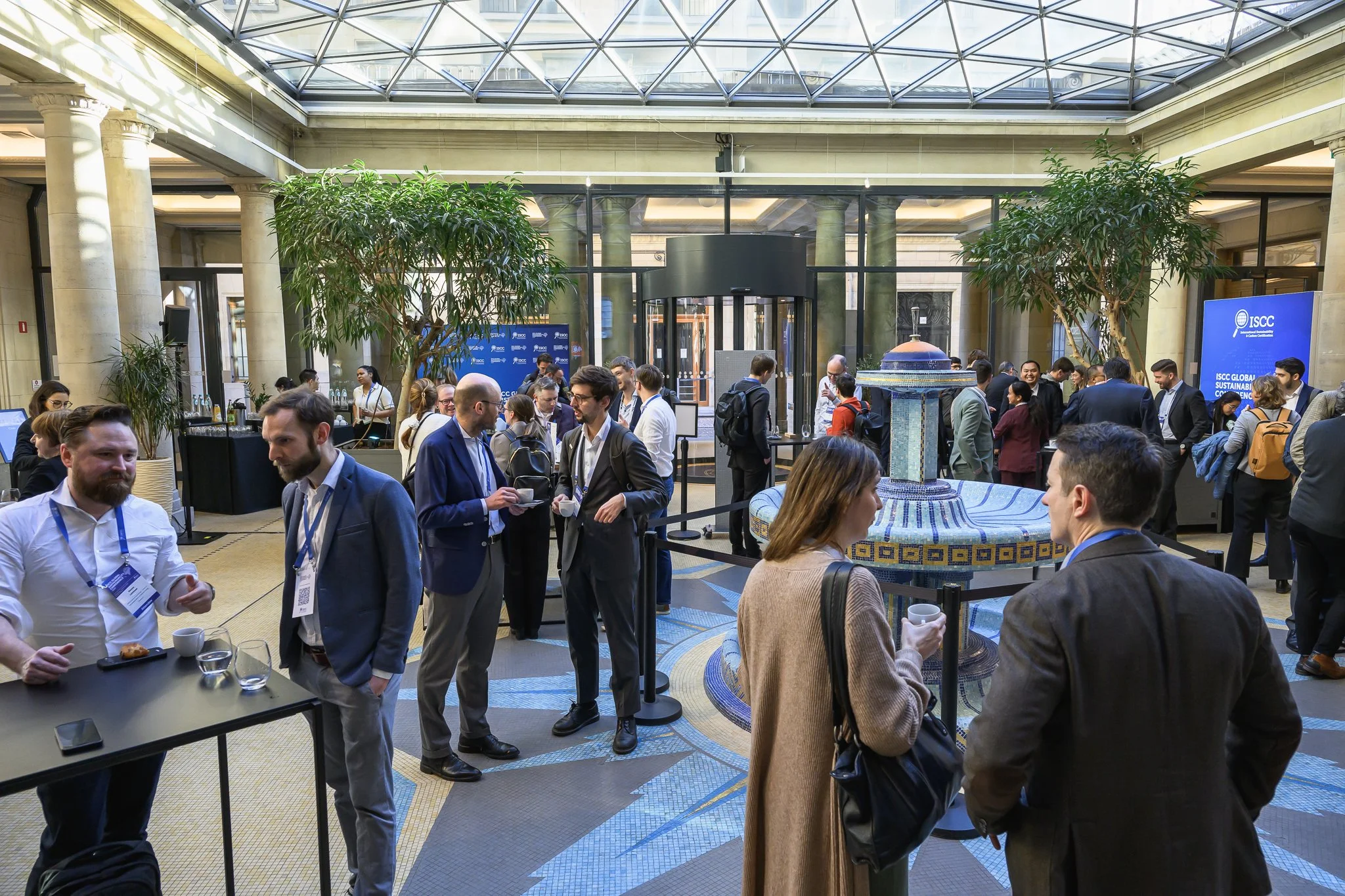 Conference participants gather in the bright lobby beneath a glass roof.
