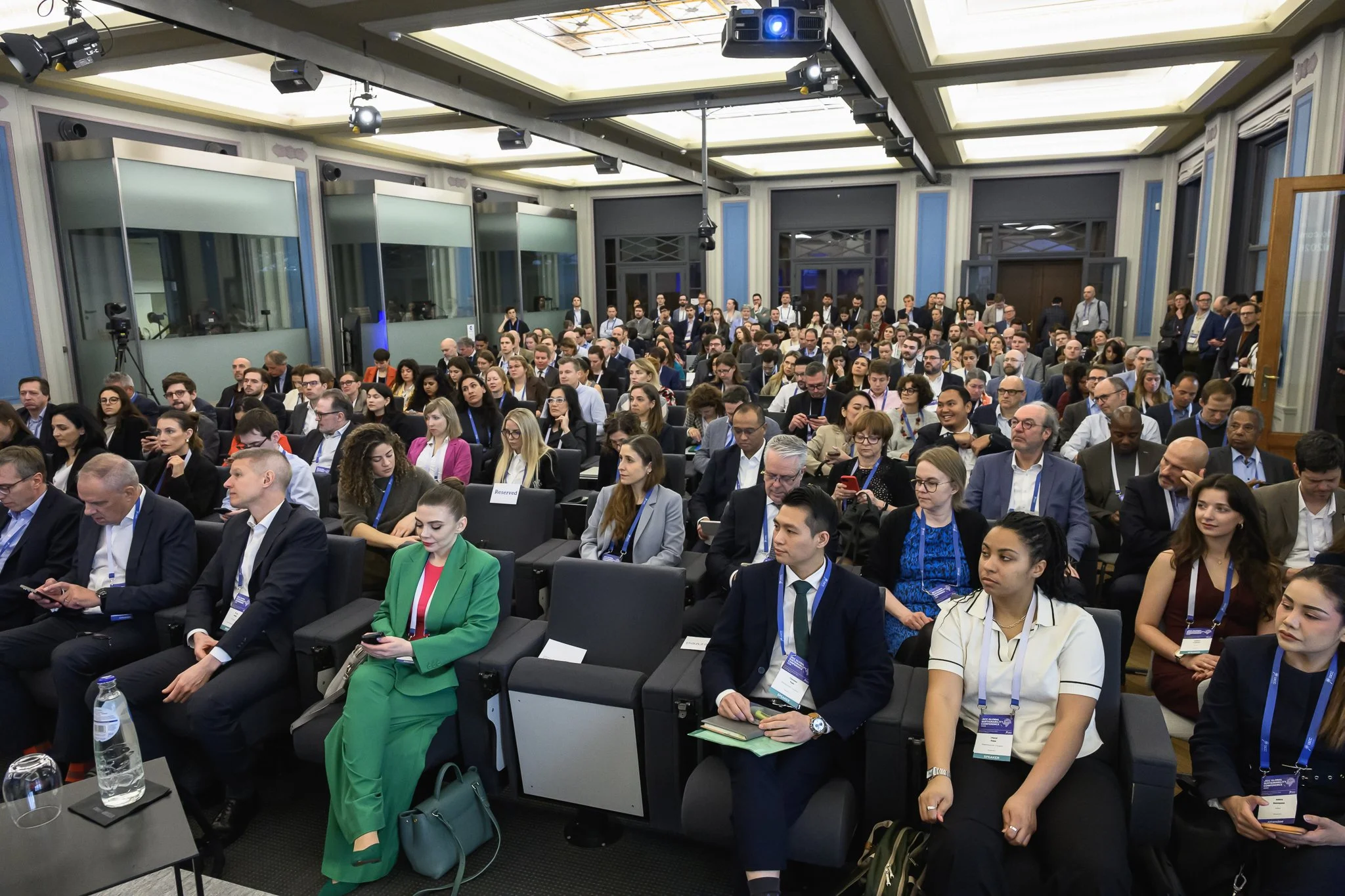 Rows of seated conference participants face the stage in a bright auditorium.