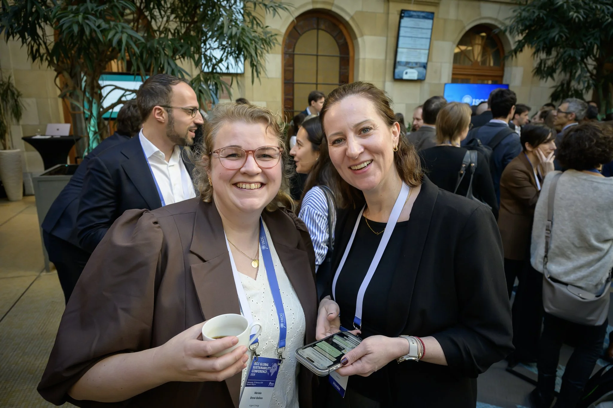 Two smiling women pose together in the conference lobby, one holding a cup.