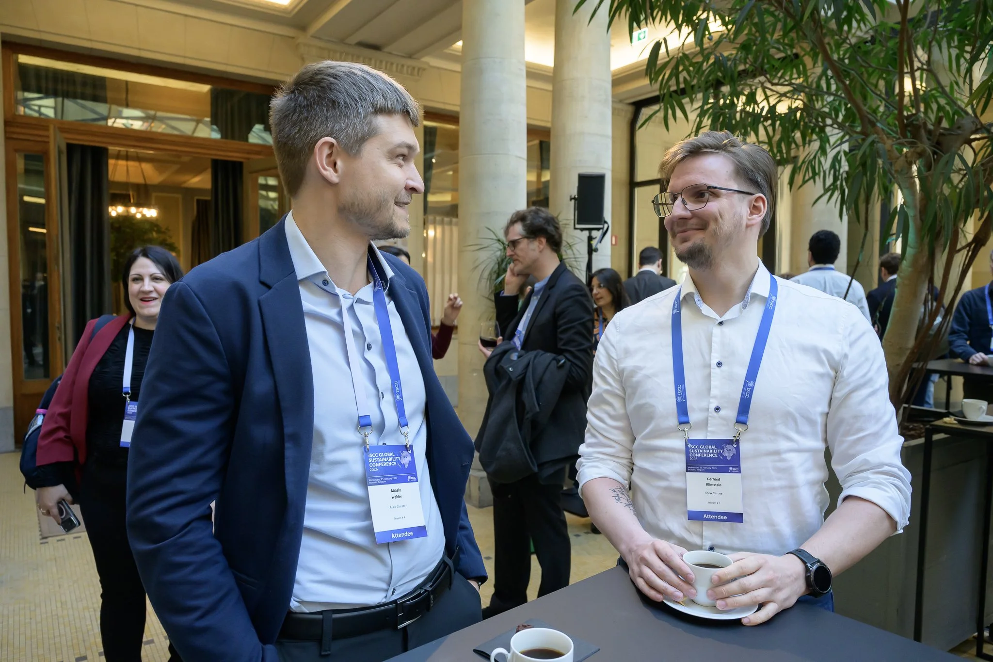 Two participants wearing lanyards converse beside a lobby table.