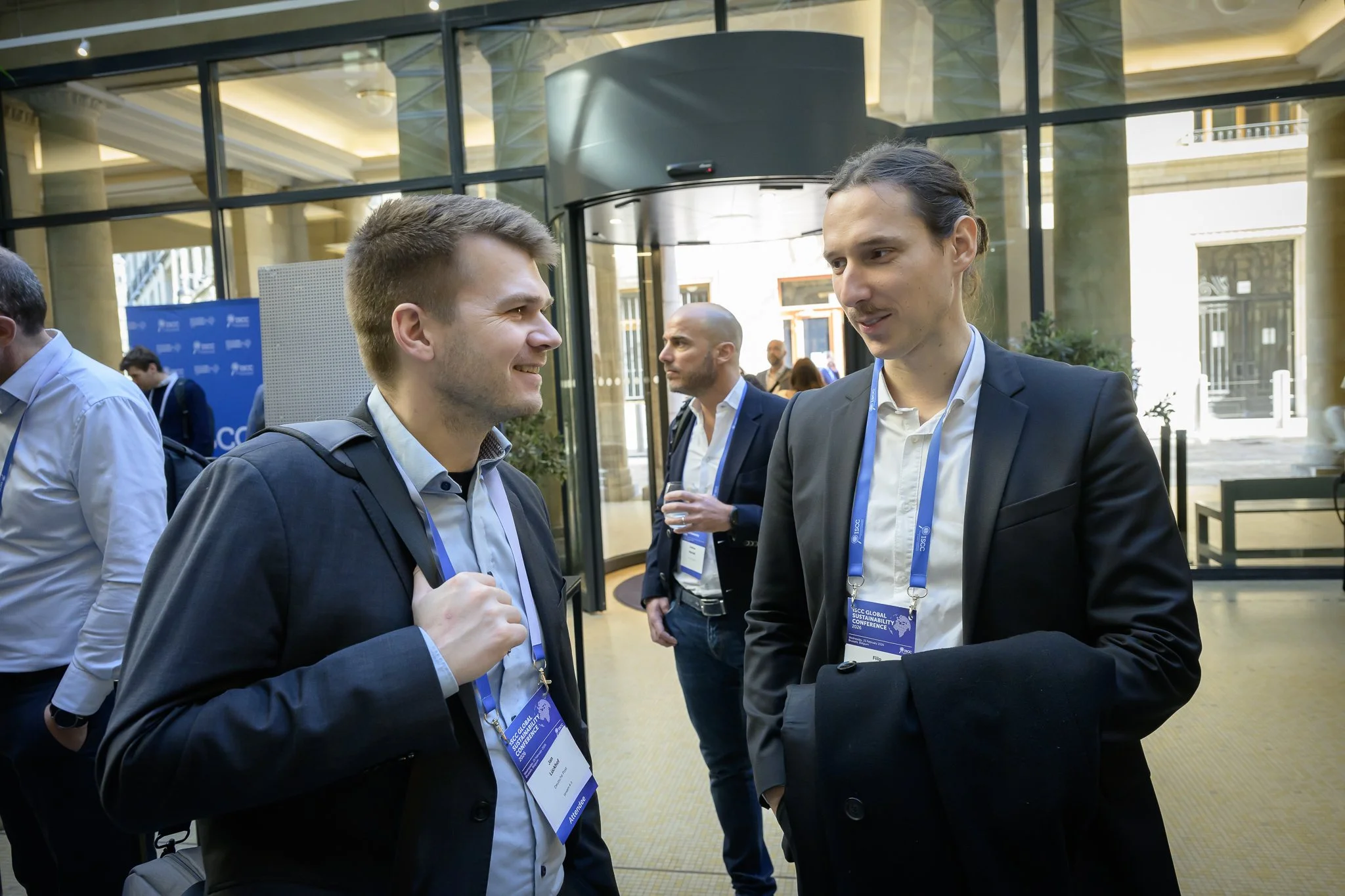 Two men wearing lanyards talk in front of the lobby entrance.