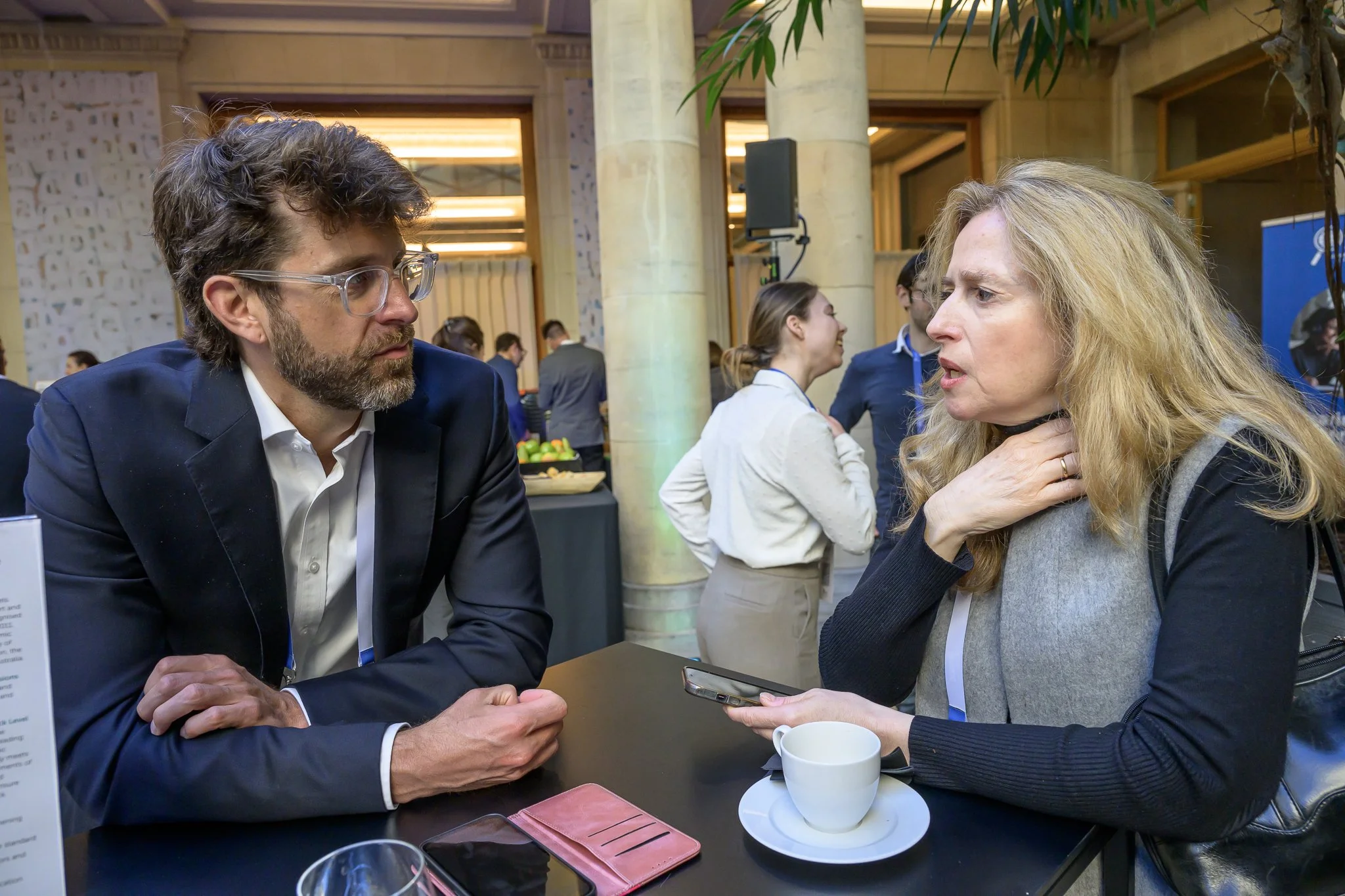 A man and a woman converse at a tall table with a cup and saucer.