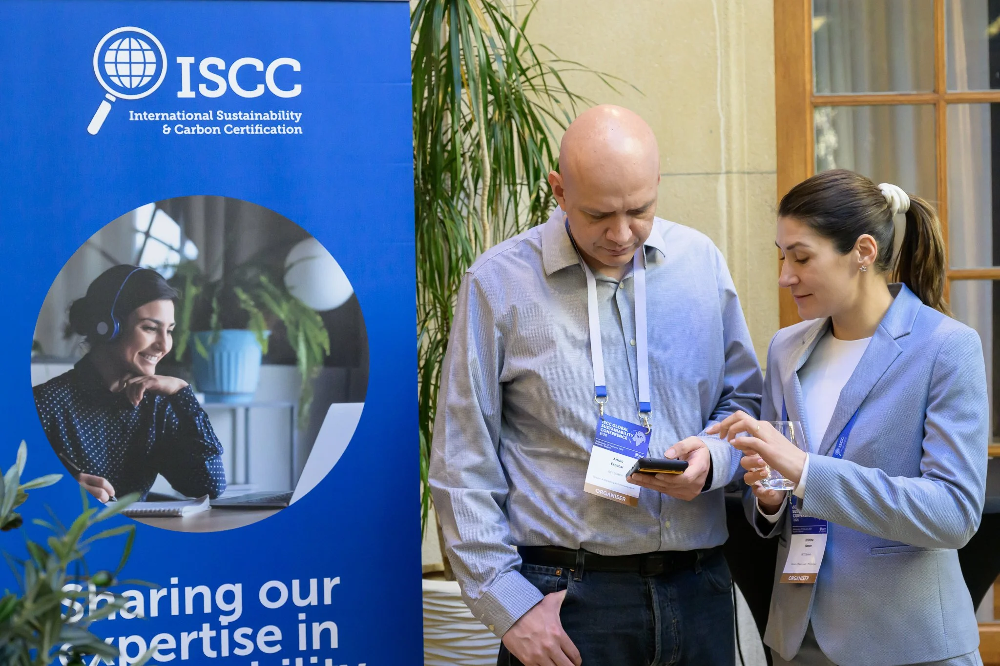 A man and a woman look together at a smartphone beside an ISCC banner.