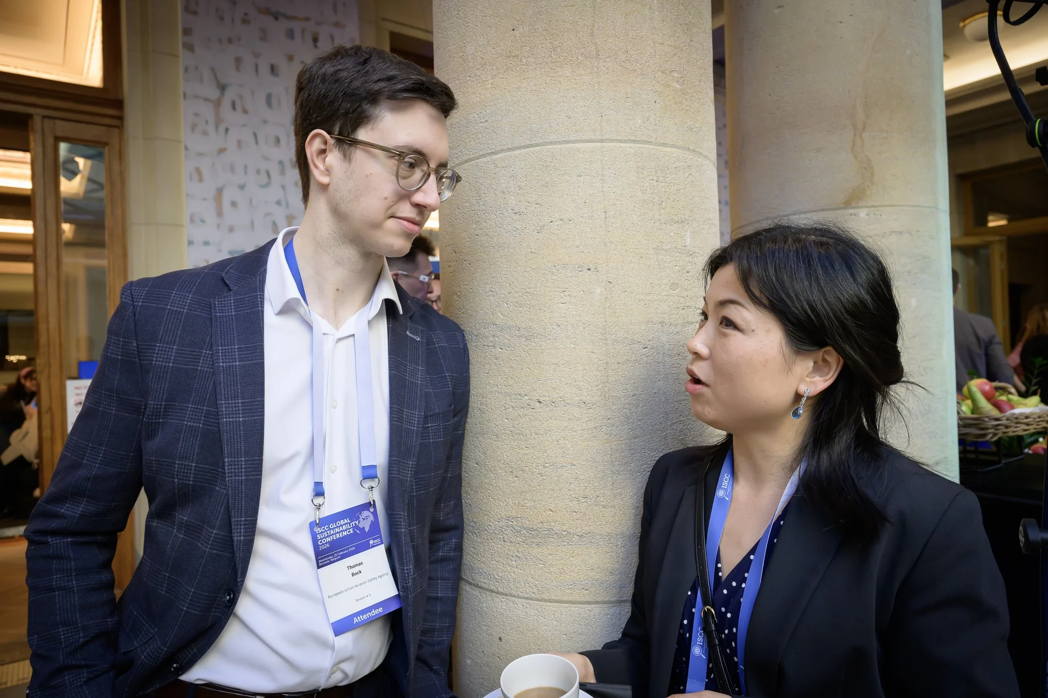 A tall man with glasses talks with a woman wearing a dark jacket.