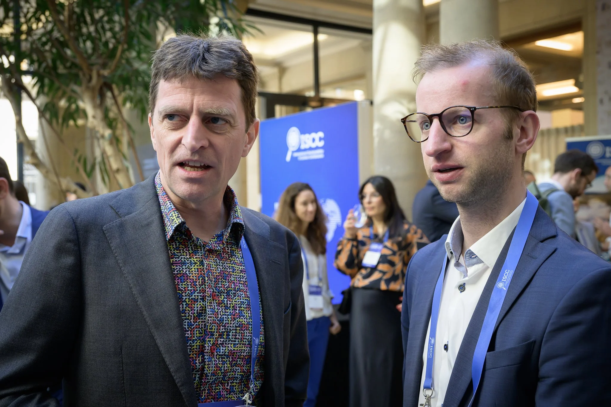 Two men wearing lanyards stand together in the conference lobby.