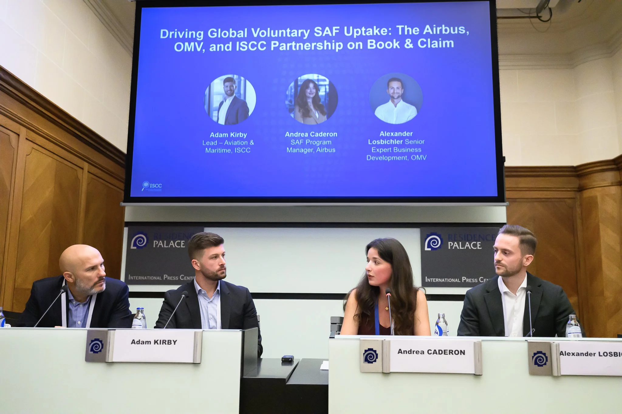 Four panel participants sit beneath a screen describing a sustainable aviation fuel partnership.
