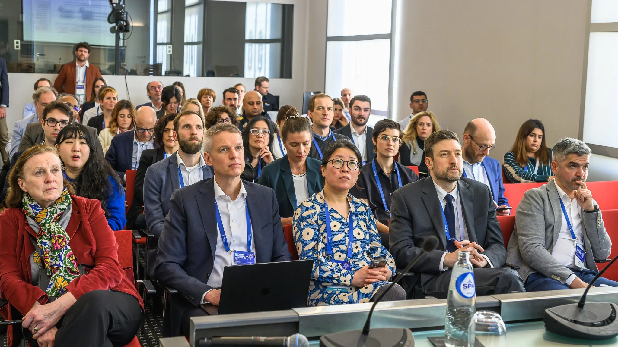 Participants sit closely together and listen in a smaller conference room.