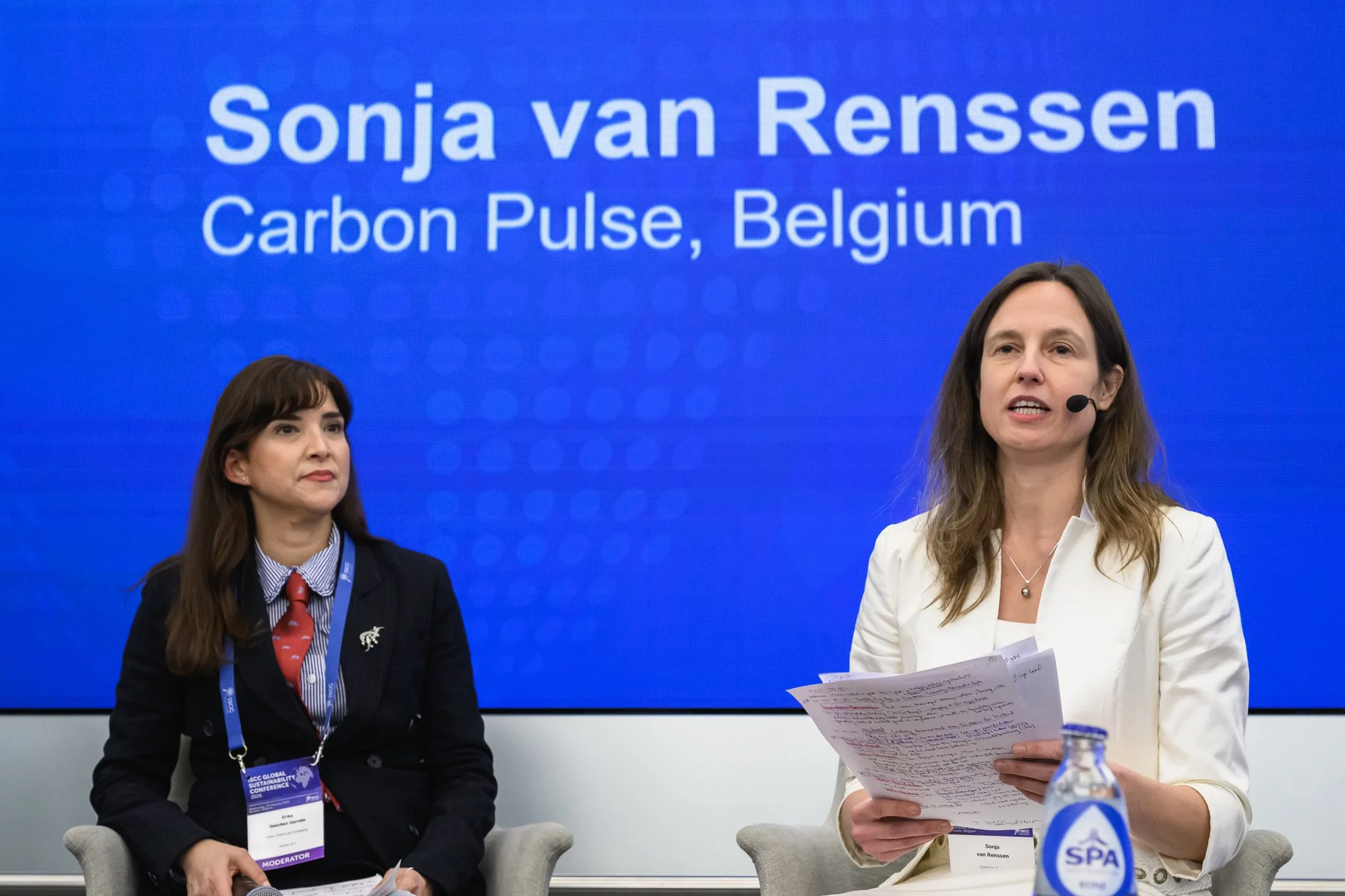 Two women sit on stage beneath a slide naming Sonja van Renssen.