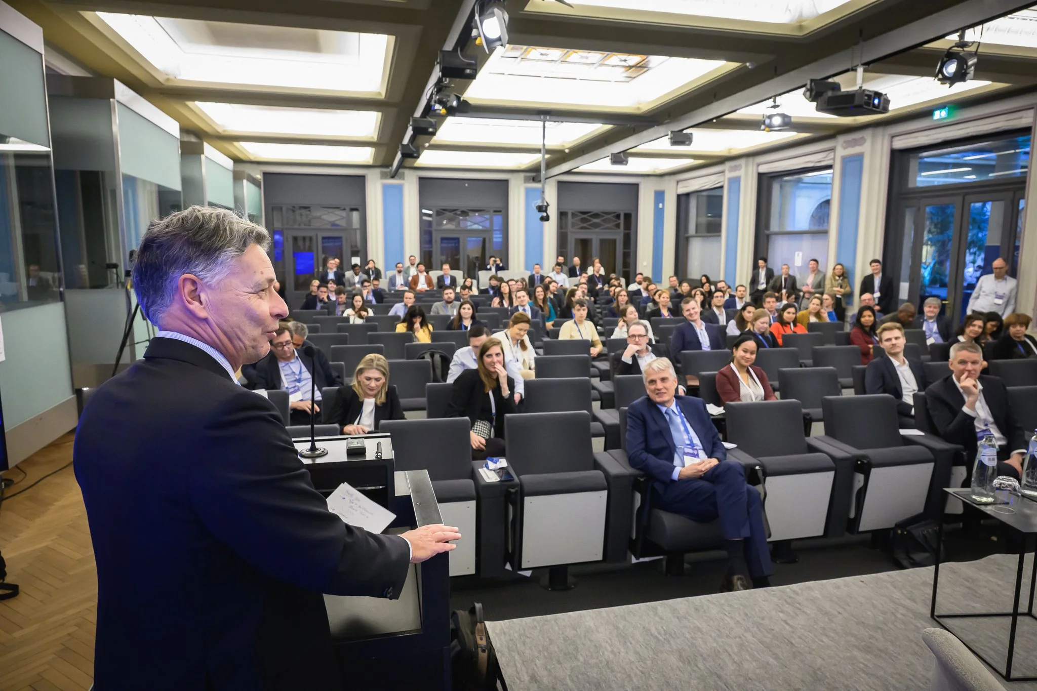 A speaker wearing a headset microphone faces the seated audience during the closing session.