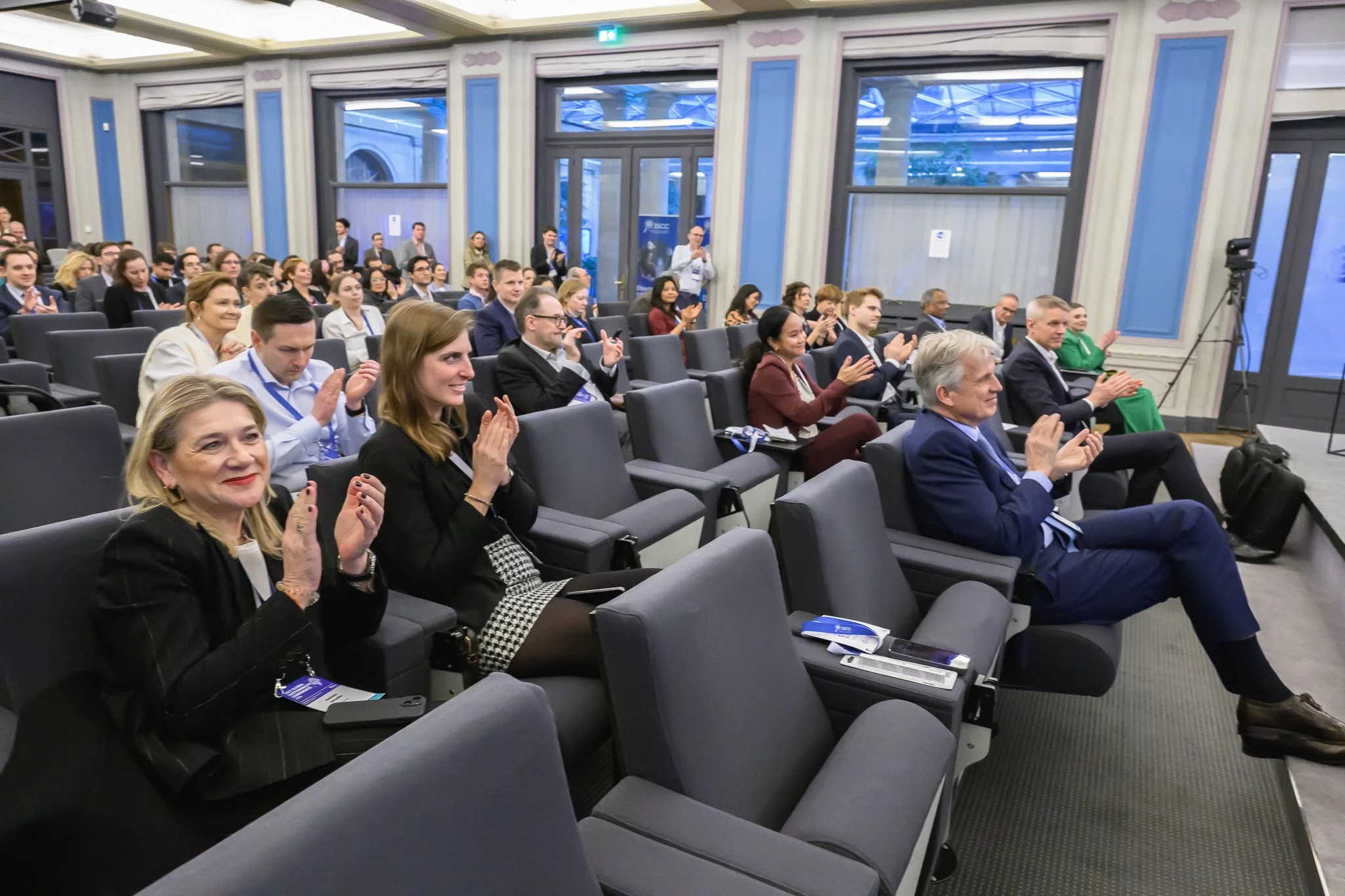 Conference participants applaud from their seats in the auditorium.