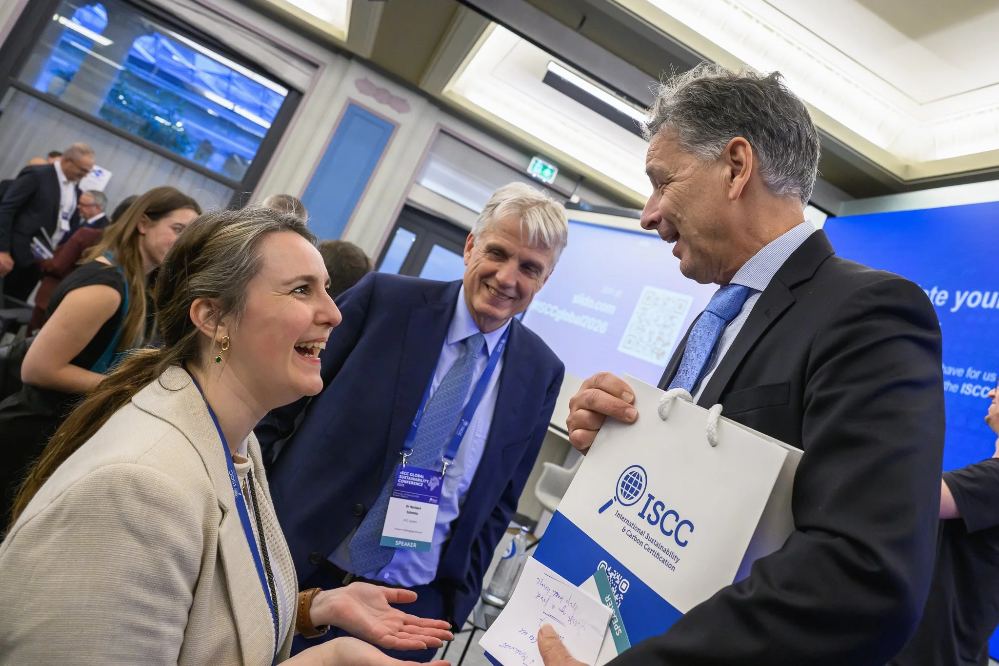 Participants laugh together near the stage, with one holding an ISCC gift bag.