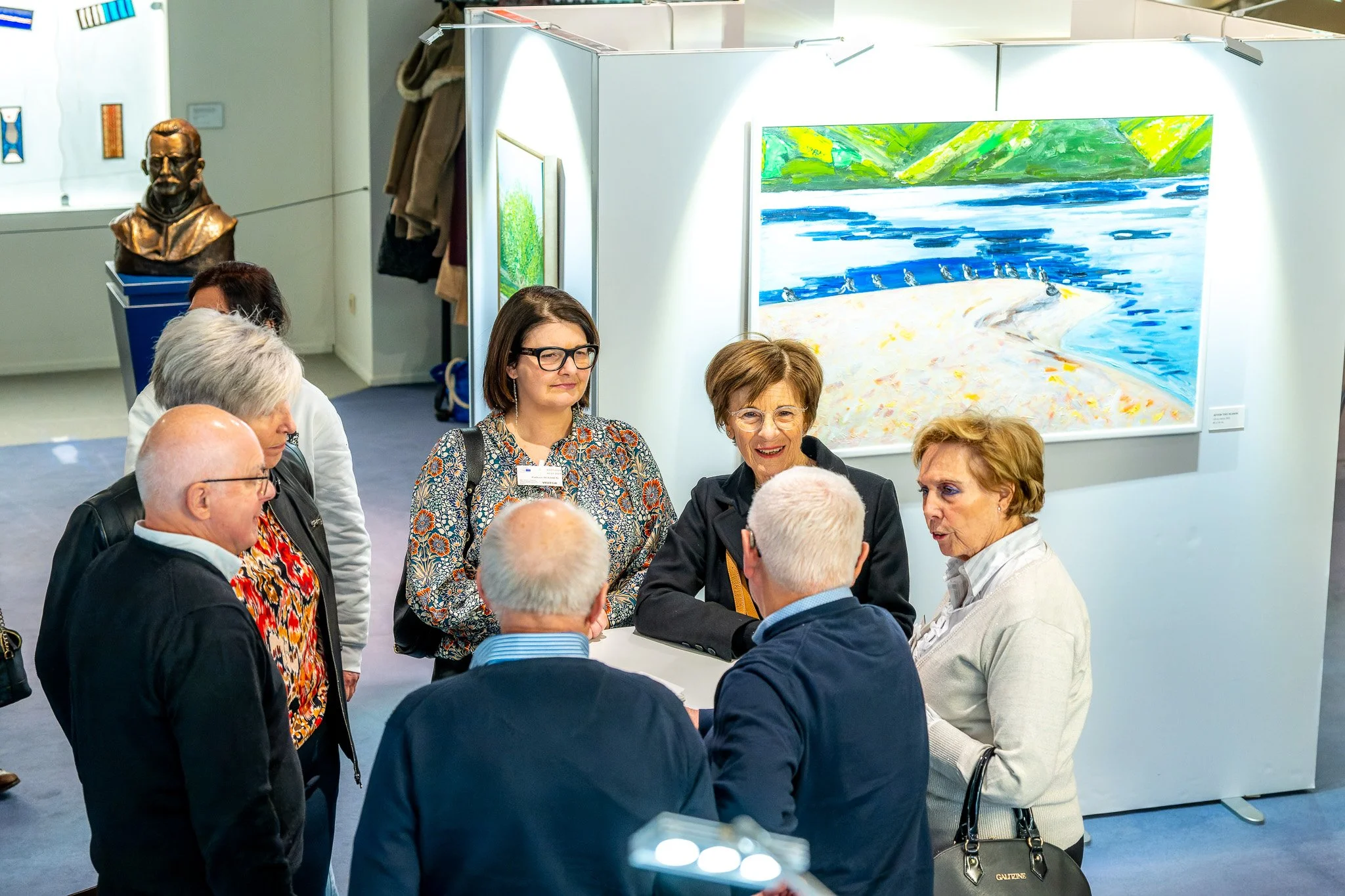 Photographie professionnelle à Bruxelles pendant une inauguration. Groupe de personnes discutant dans une galerie d'art avec des peintures exposées.