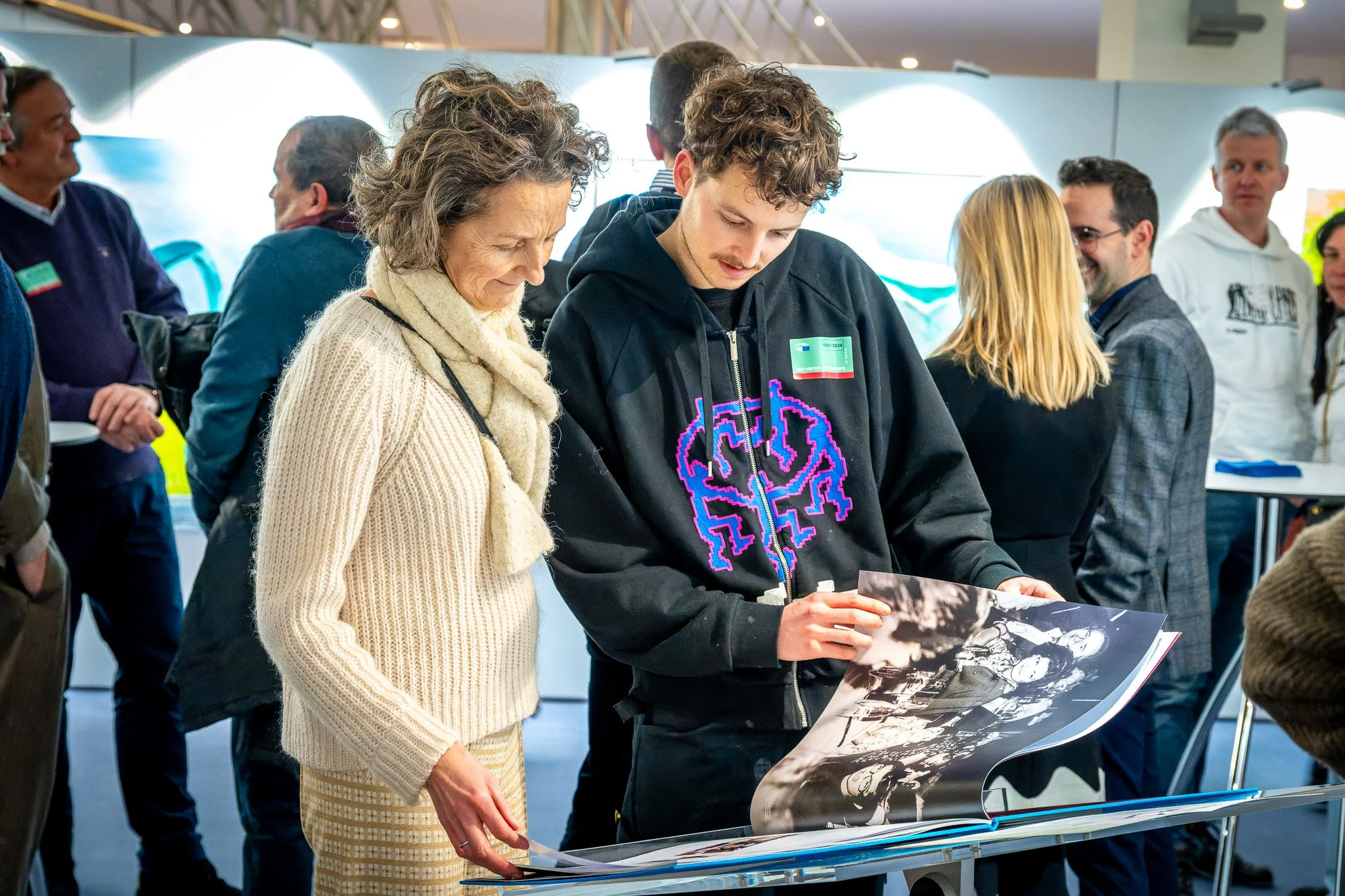 Photo d'un event à Bruxelles.Un homme et une femme regardent une photo en noir et blanc dans un environnement avec plusieurs personnes en arrière-plan.