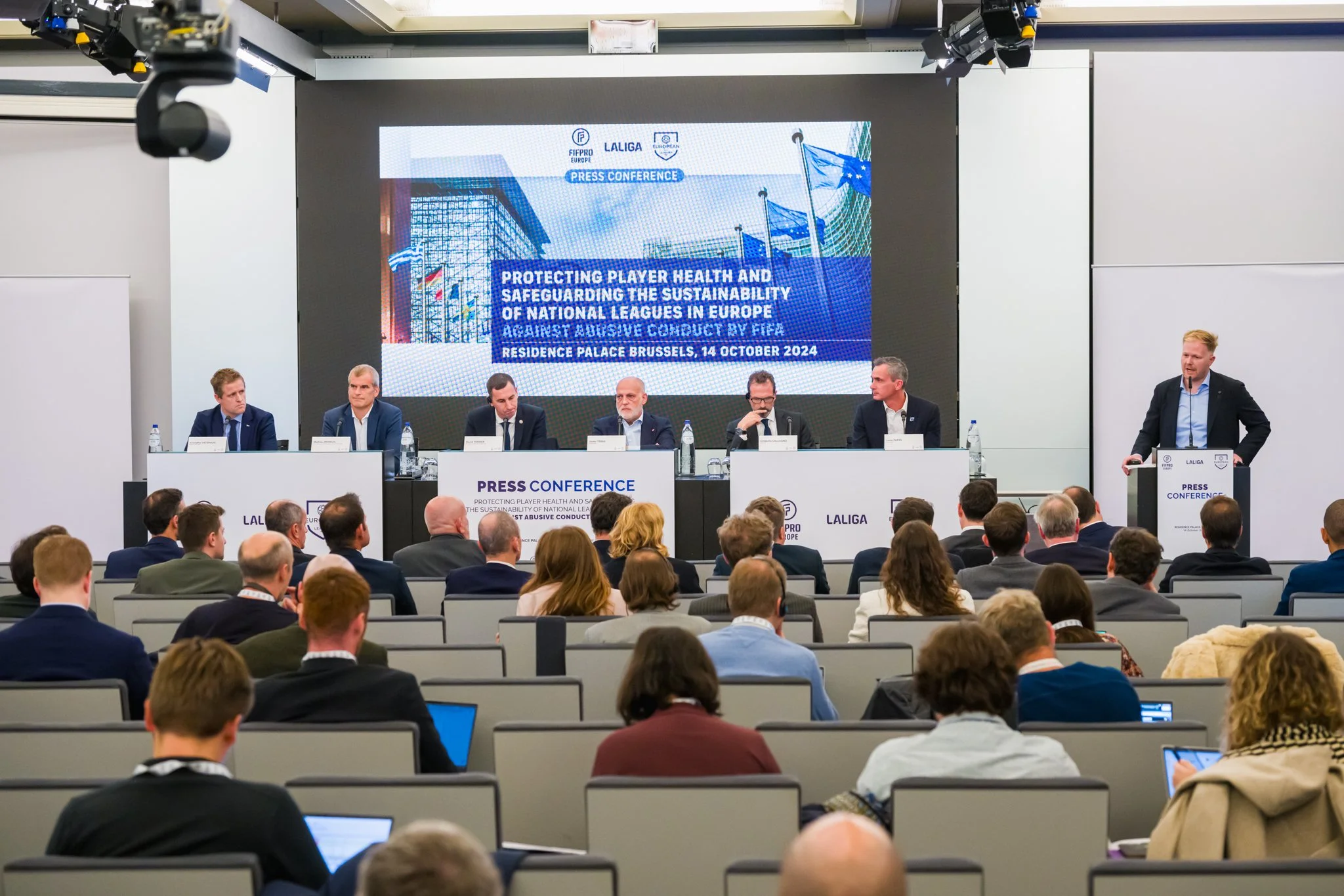 Conférence de presse à Bruxelles sur la protection de la santé des joueurs et la durabilité des ligues nationales européennes, organisée par la FIFPRO et LaLiga, avec plusieurs intervenants assis à une table devant un public.