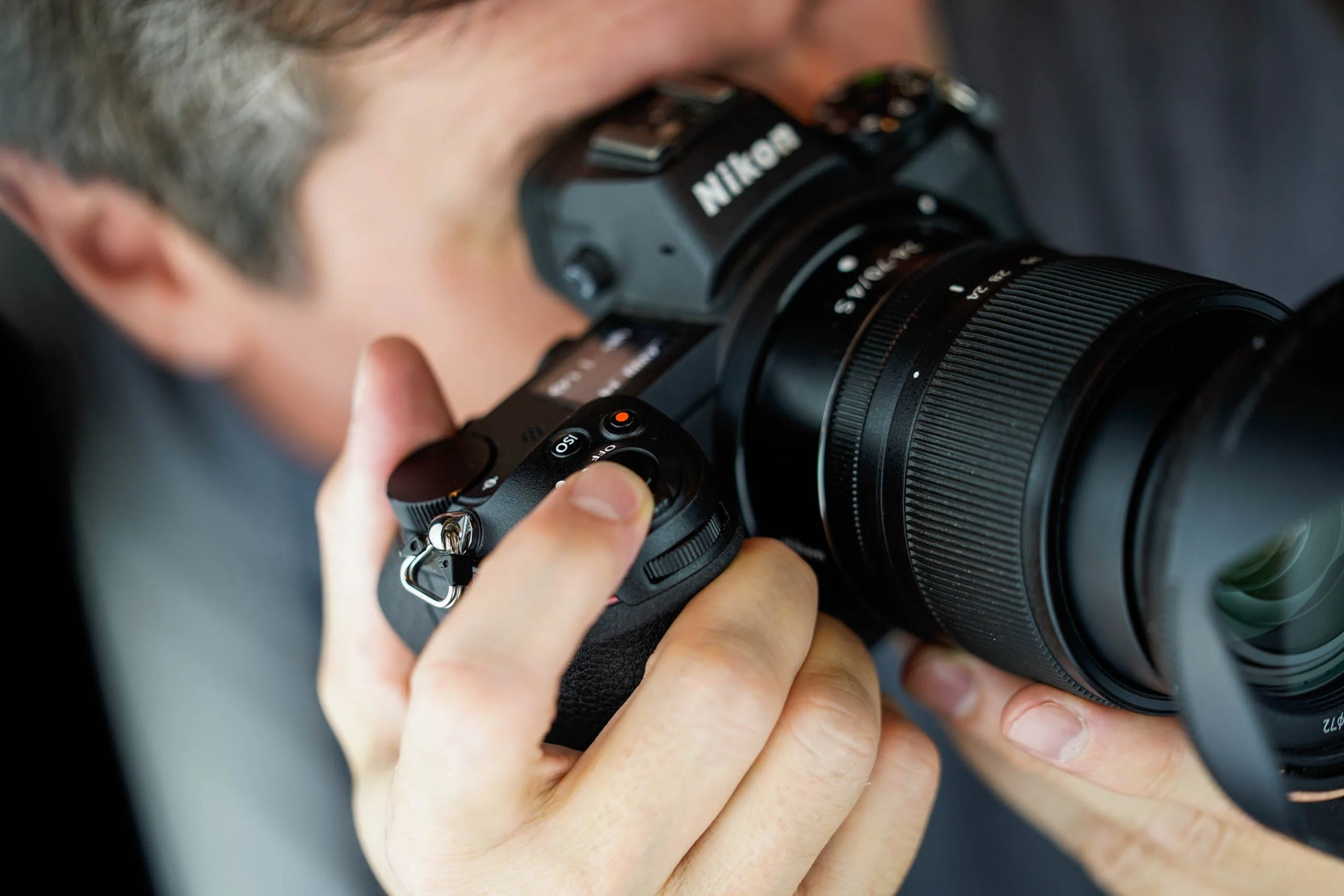 A close-up of a photographer looking through the viewfinder of his camera, which is fitted with a long lens.