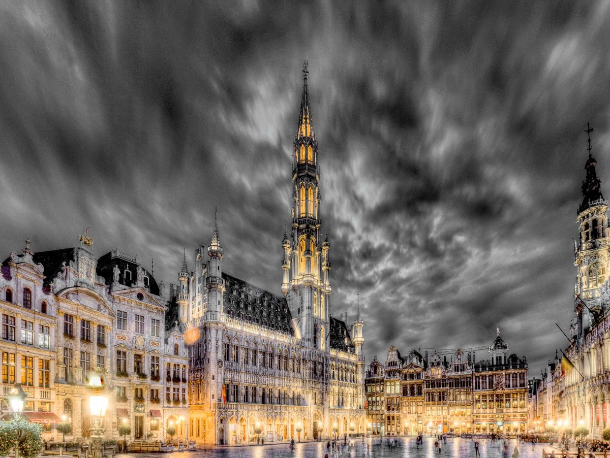 Vue nocturne de la Grand-Place de Bruxelles avec bâtiments historiques et ciel nuageux.
