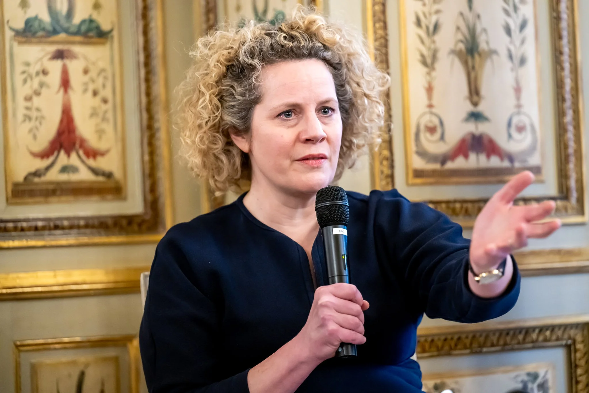 A woman speaking into a microphone in a decorated room.
