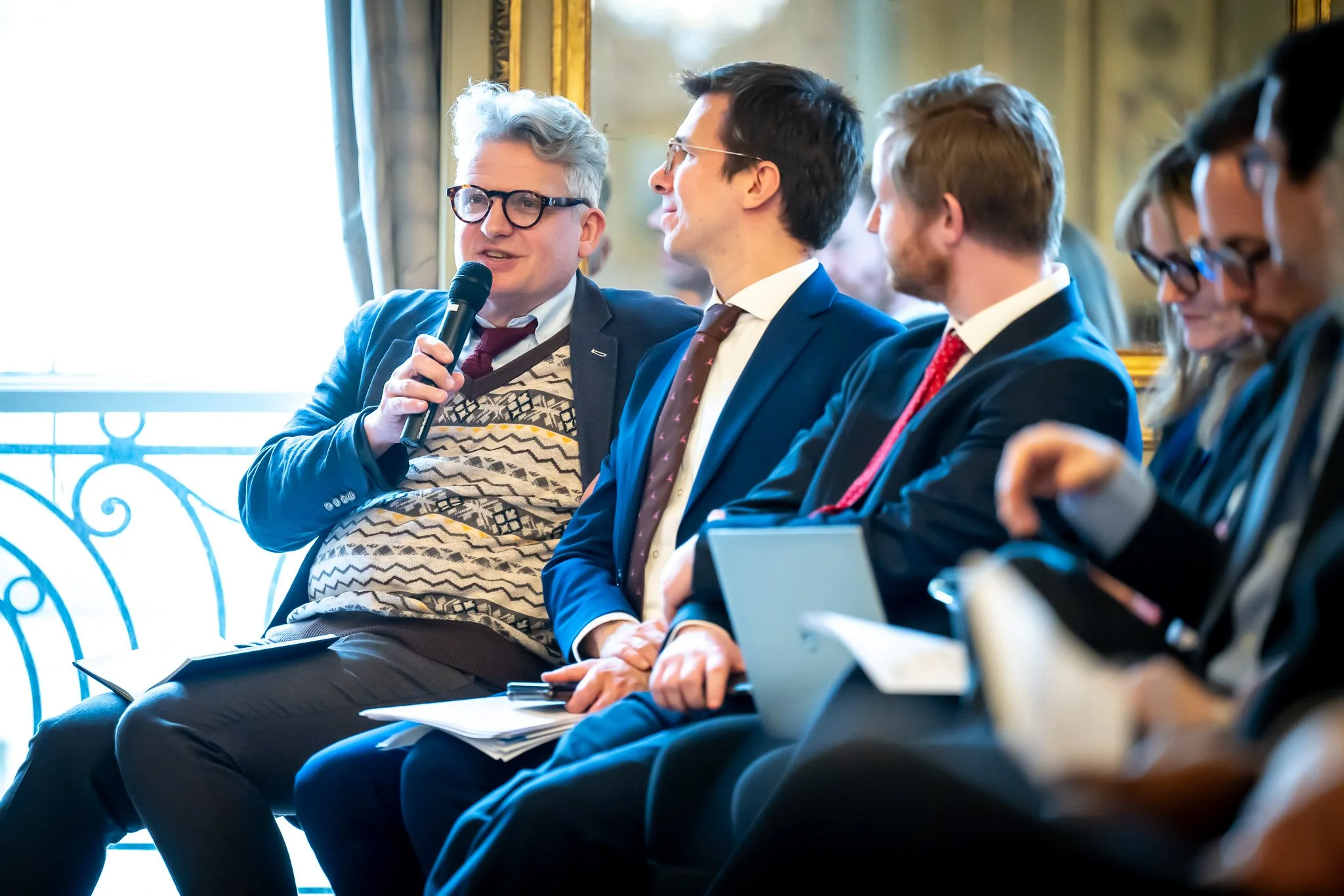 A group of people in formal attire at a conference; a man holding a microphone.