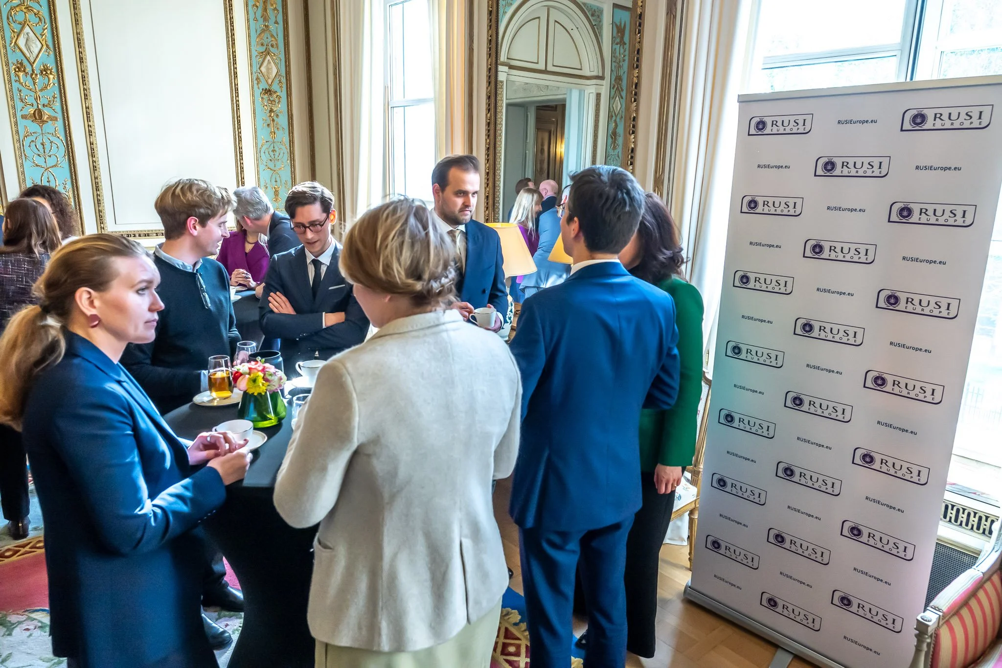 A group of people chatting at a formal event, with a RUSI banner in the background.