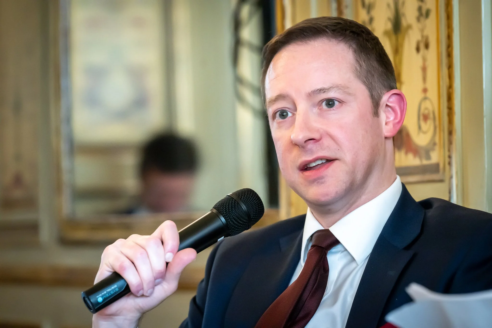 A man in a suit is speaking into a microphone.