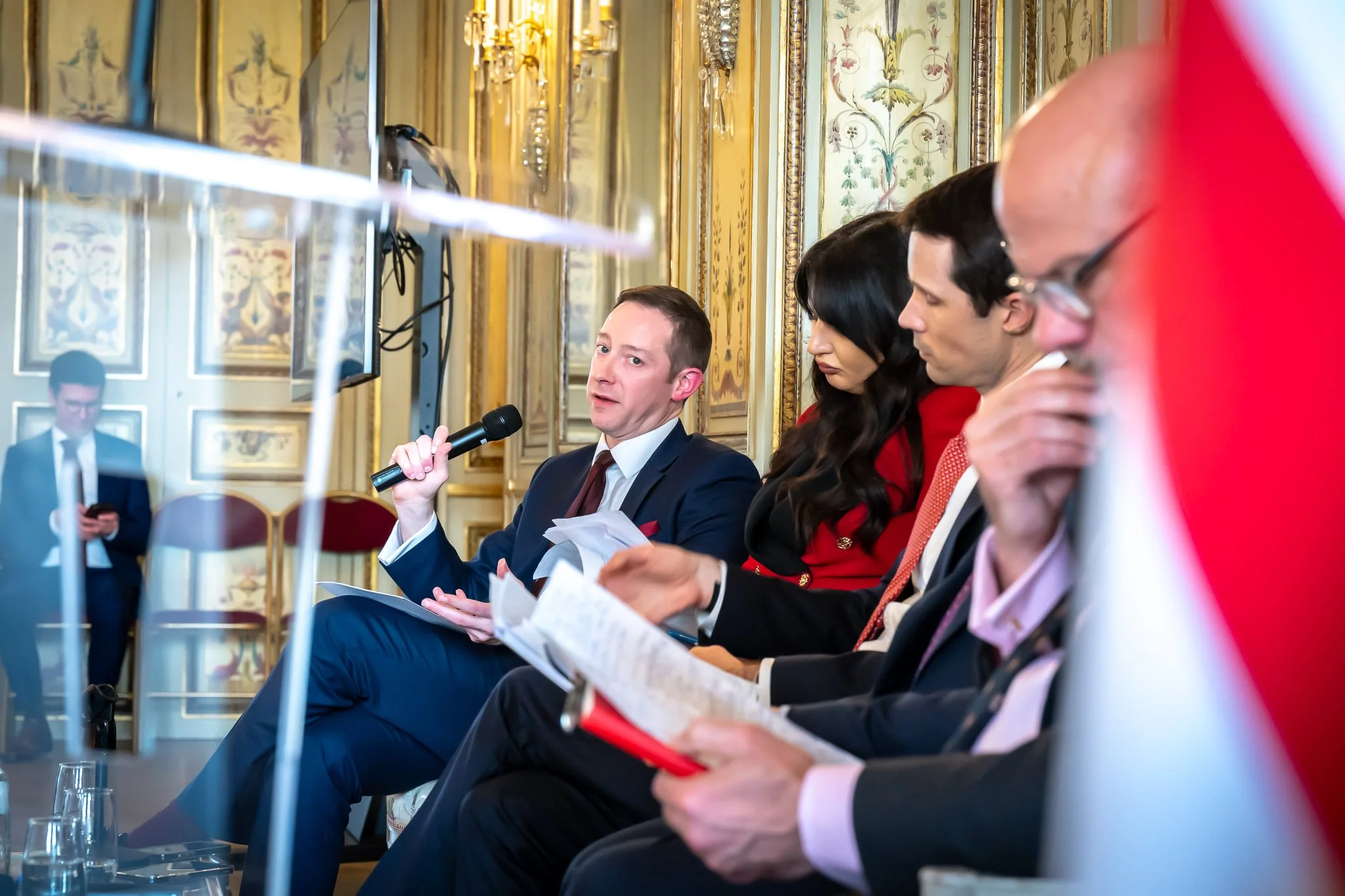 Panel participants listen as a seated man speaks into a microphone.