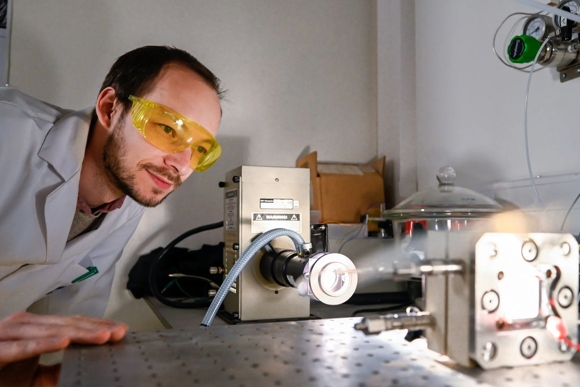 Photographie corporate d'un scientifique portant des lunettes de protection jaunes observe un appareil en laboratoire.