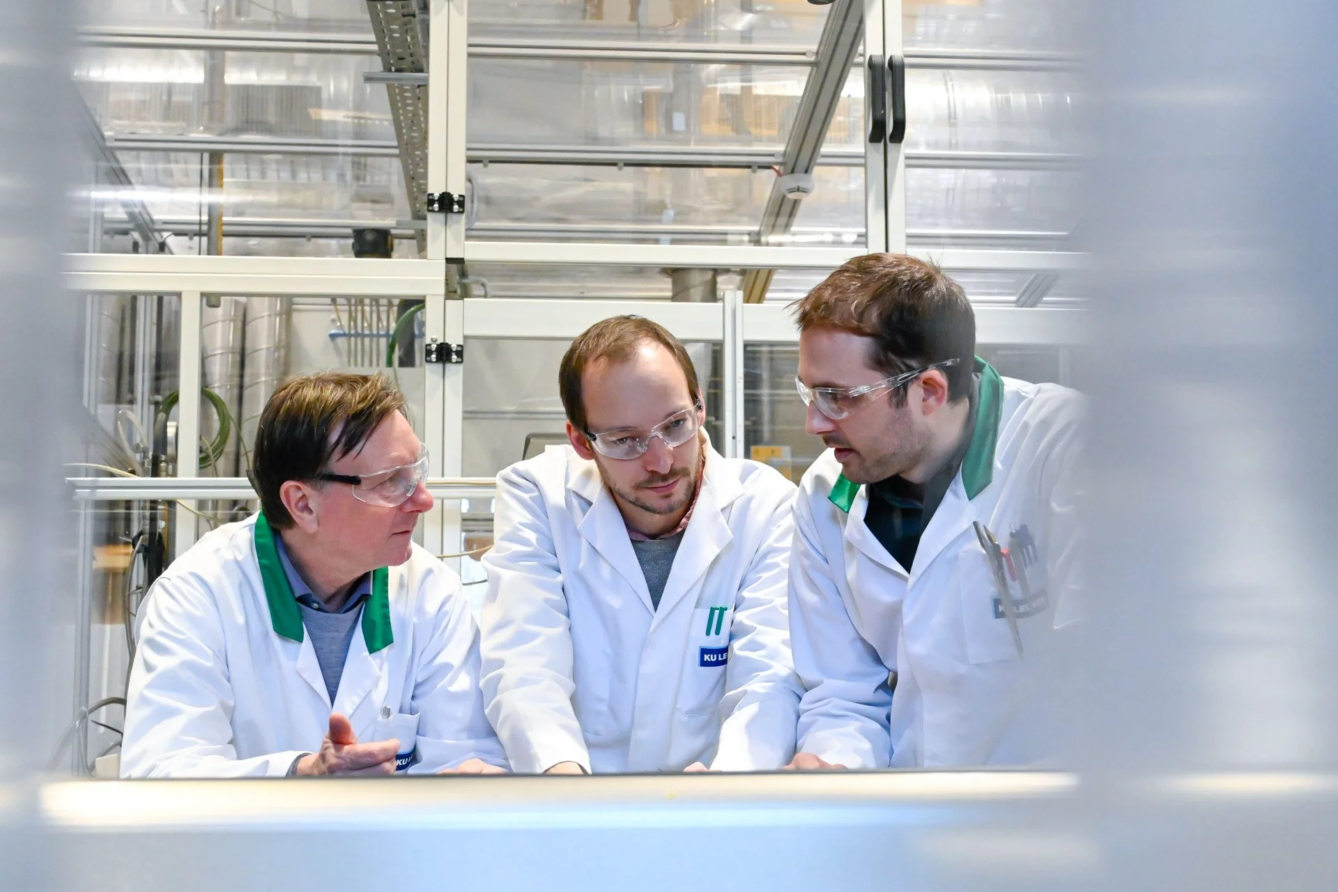 Photo coporate dans une université qui illustre trois scientifiques portant des blouses blanches et des lunettes de protection discutent dans un laboratoire moderne.