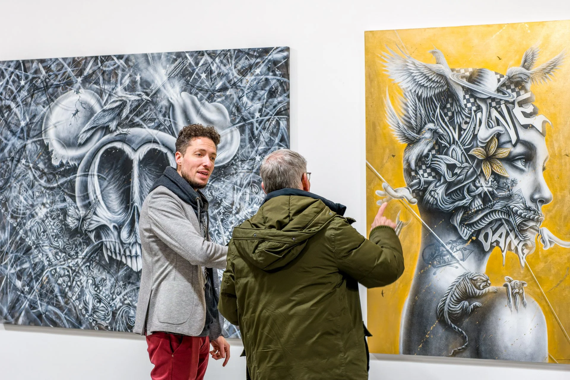 Deux hommes discutent devant deux tableaux artistiques dans une galerie.